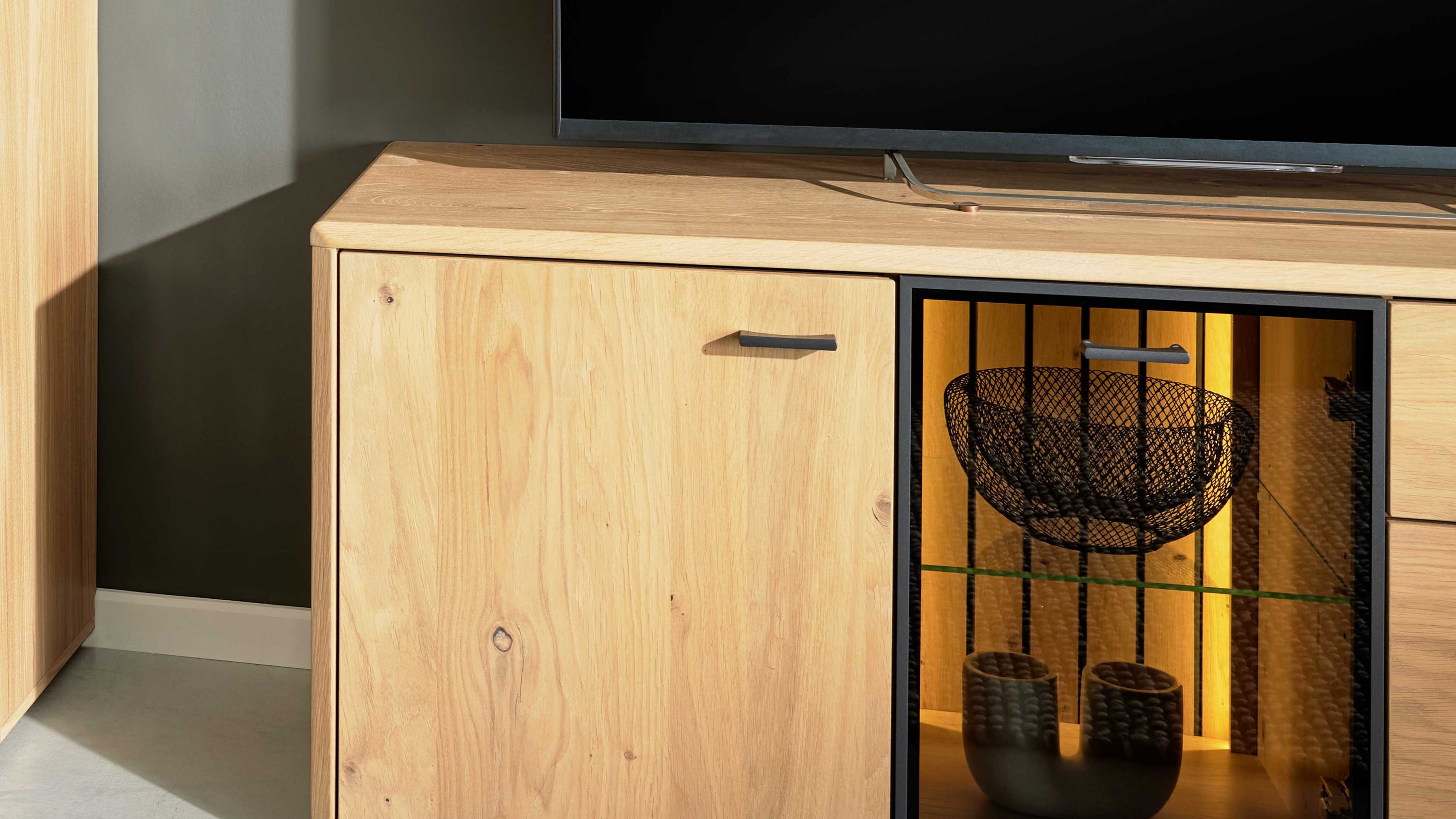 Wohnzimmerschrank mit zwei Türen eine Holztür und eine Glastür mit schwarzem Rahmen und integrierter Beleuchtung