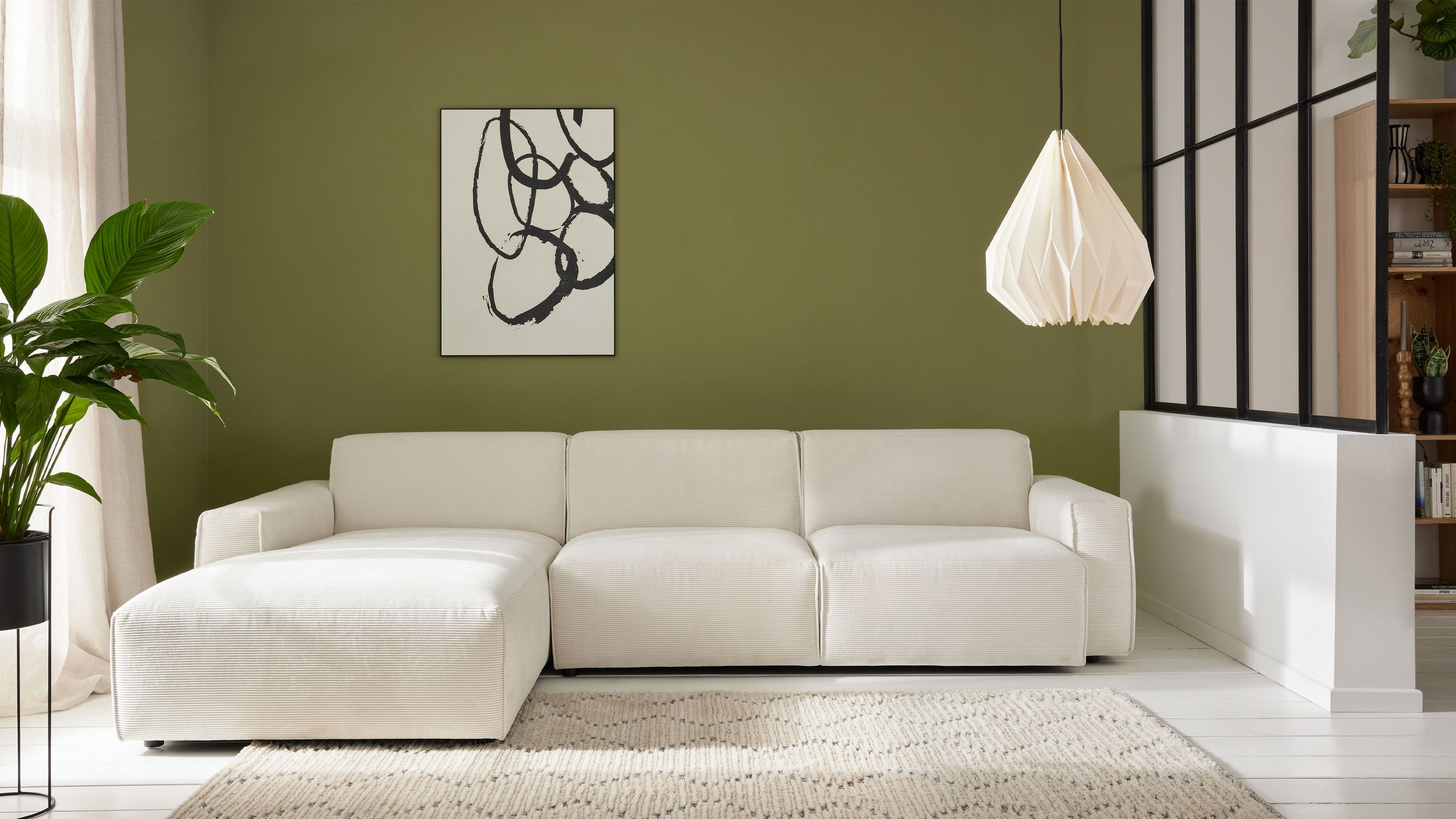 Ecksofa mit linker Chaiselongue in weißem Stoff vor grüner Wand mit abstraktem Bild