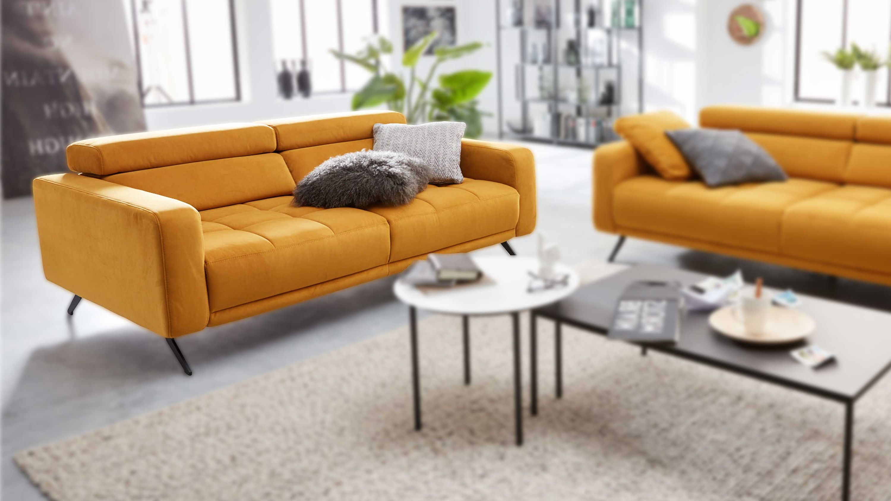 Dreisitziges Sofa in curryfarben mit niedriger Rückenlehne und schwarzen Metallbeinen mit zwei grauen Kissen