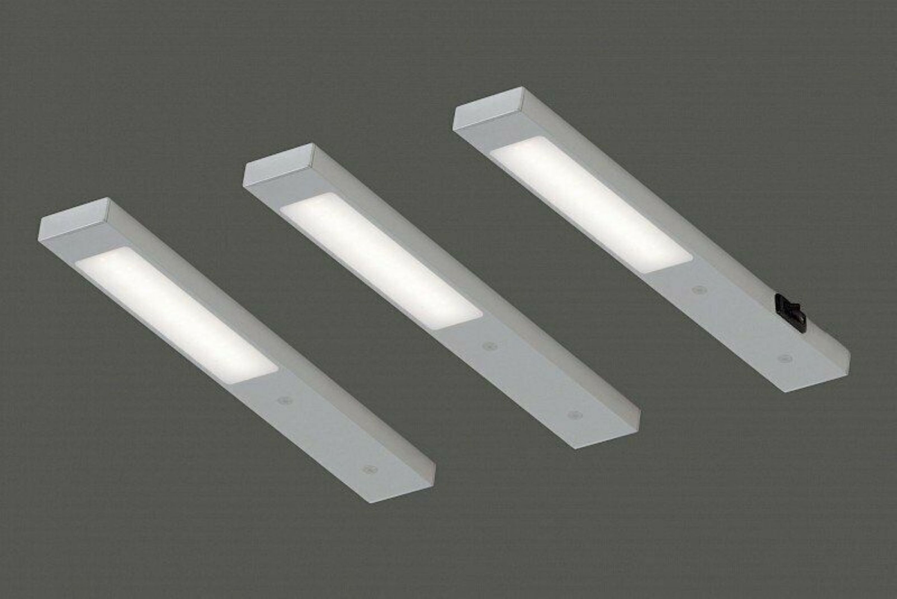 Drei rechteckige Deckenleuchten mit weißem Licht, eine mit schwarzem Bauteil, auf dunklem Hintergrund montiert.