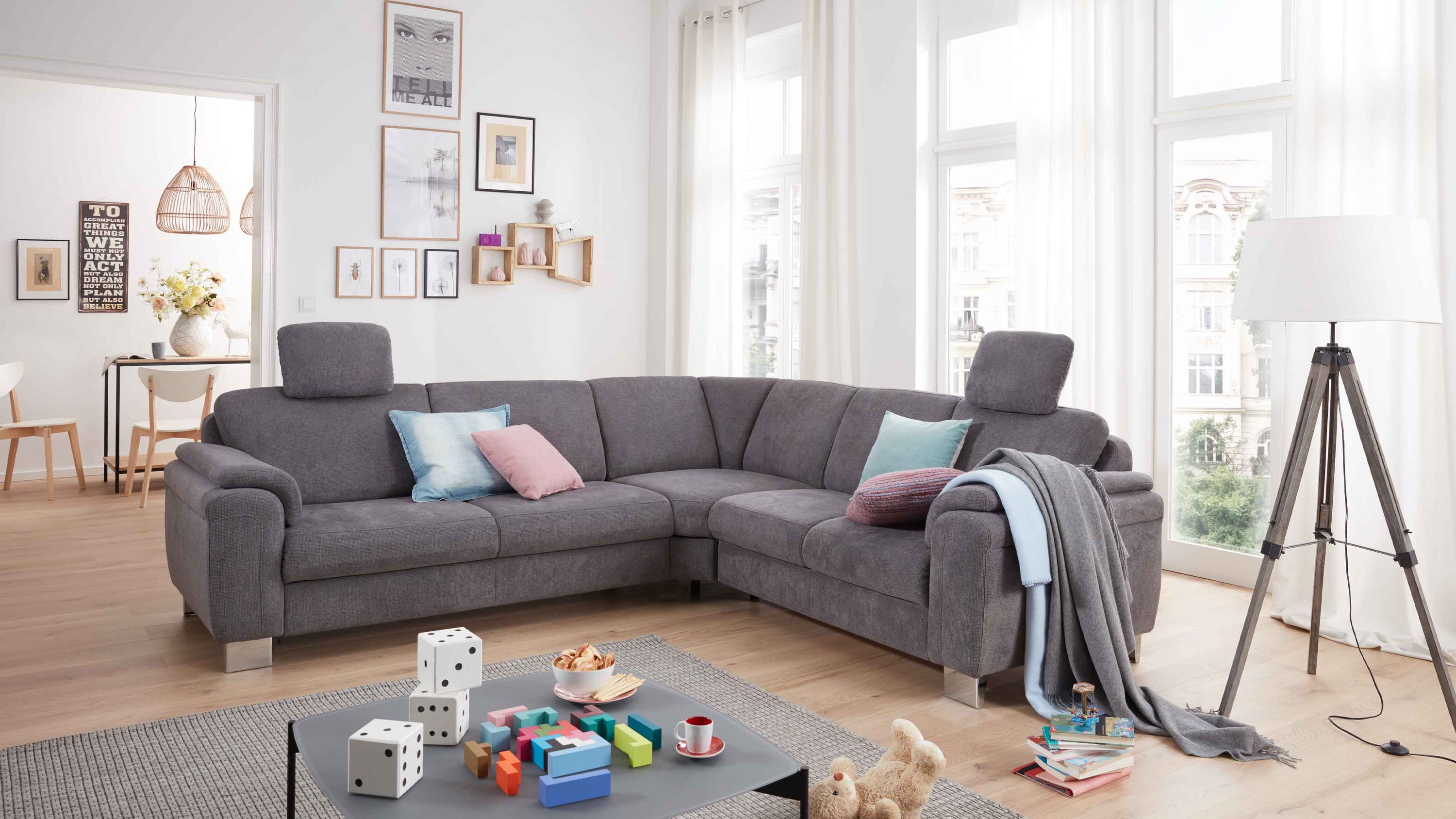 Ecksofa mit grauem Bezug zwei Kopfstützen und Chromfüßen in hellem Wohnzimmer mit Teppich und Stehlampe