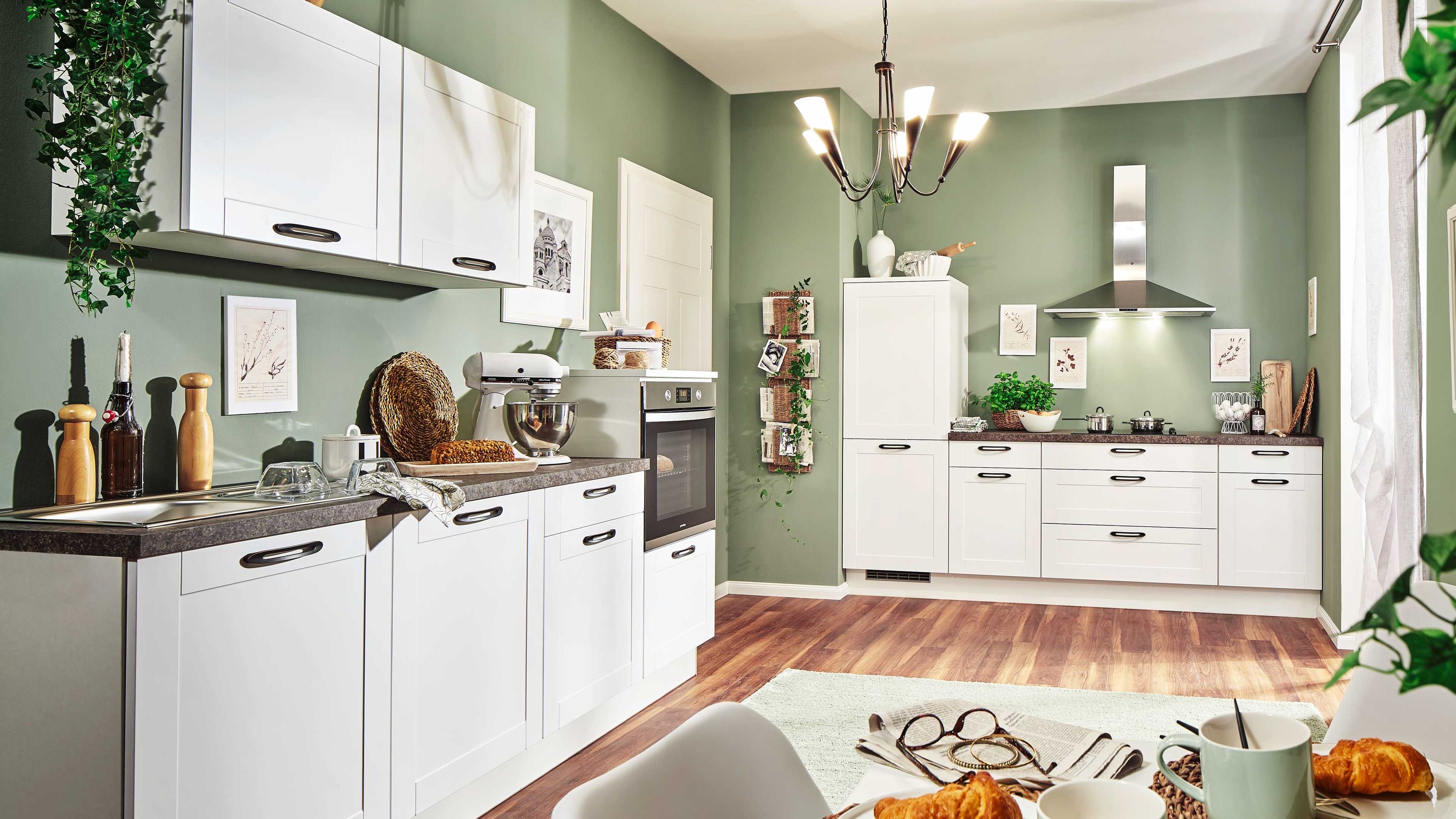Weiße Küche mit grünem Akzent und gedecktem Tisch Weiße Küche mit grüner Wand Holzboden Esstisch mit Speisen Küchenutensilien Fensterlicht moderne Ausstattung.