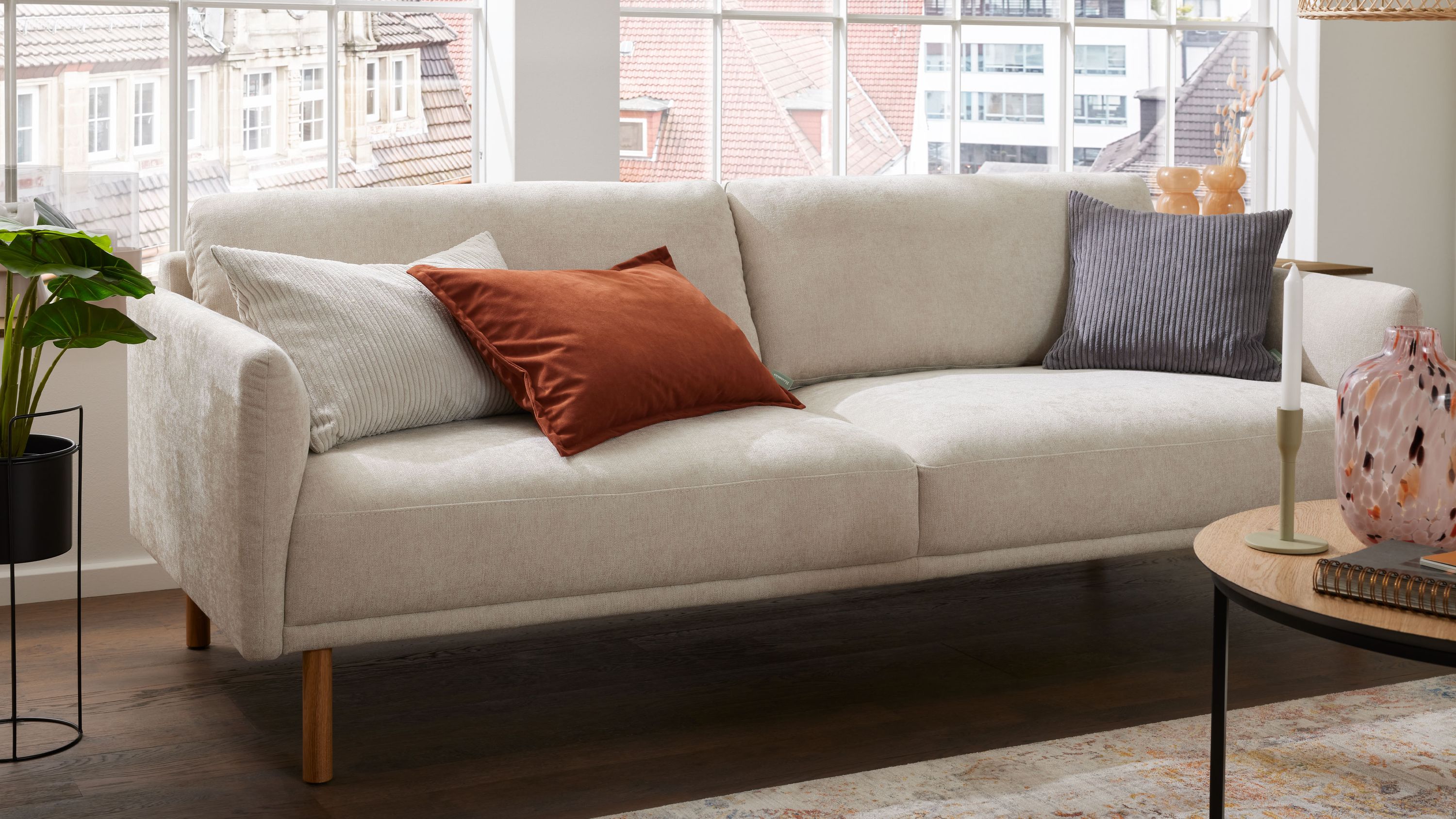 Dreisitziges Sofa mit naturfarbenem Strukturbezug und Holzfüßen dekoriert mit drei Kissen in verschiedenen Farben