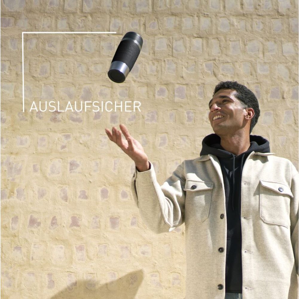 Emsa Travel Mug – auslaufsicherer Becher für sorgenfreien Genuss unterwegs Lachender Mann wirft schwarzen Emsa Travel Mug vor hellem Stein-Hintergrund, Text: Auslaufsicher