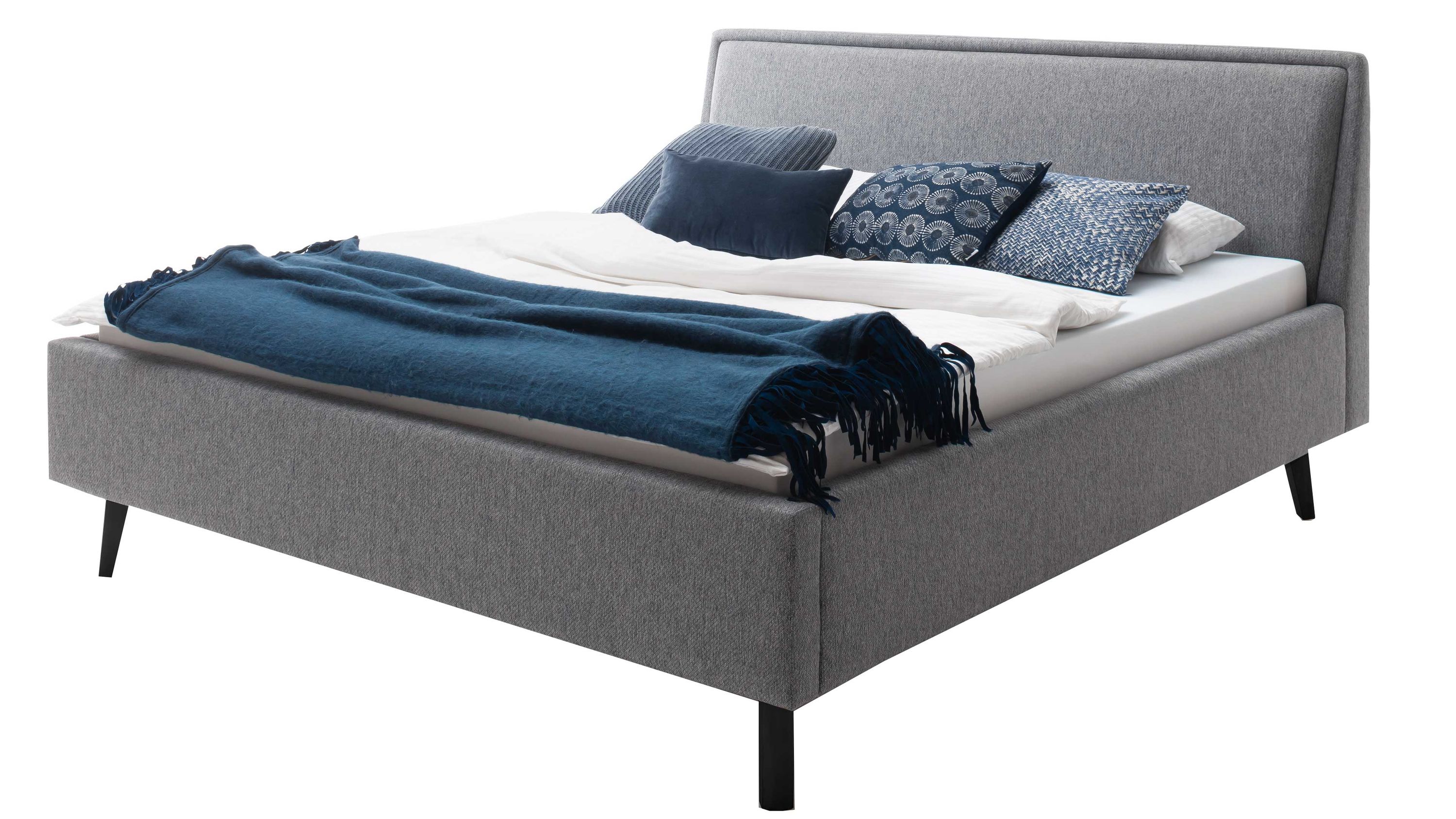Graues Polsterbett mit schwarzem Holzfuß Polsterbett mit grauem Bezug gepolstertem Kopfteil und schwarzen Holzfüßen mit Decke und Kissen belegt