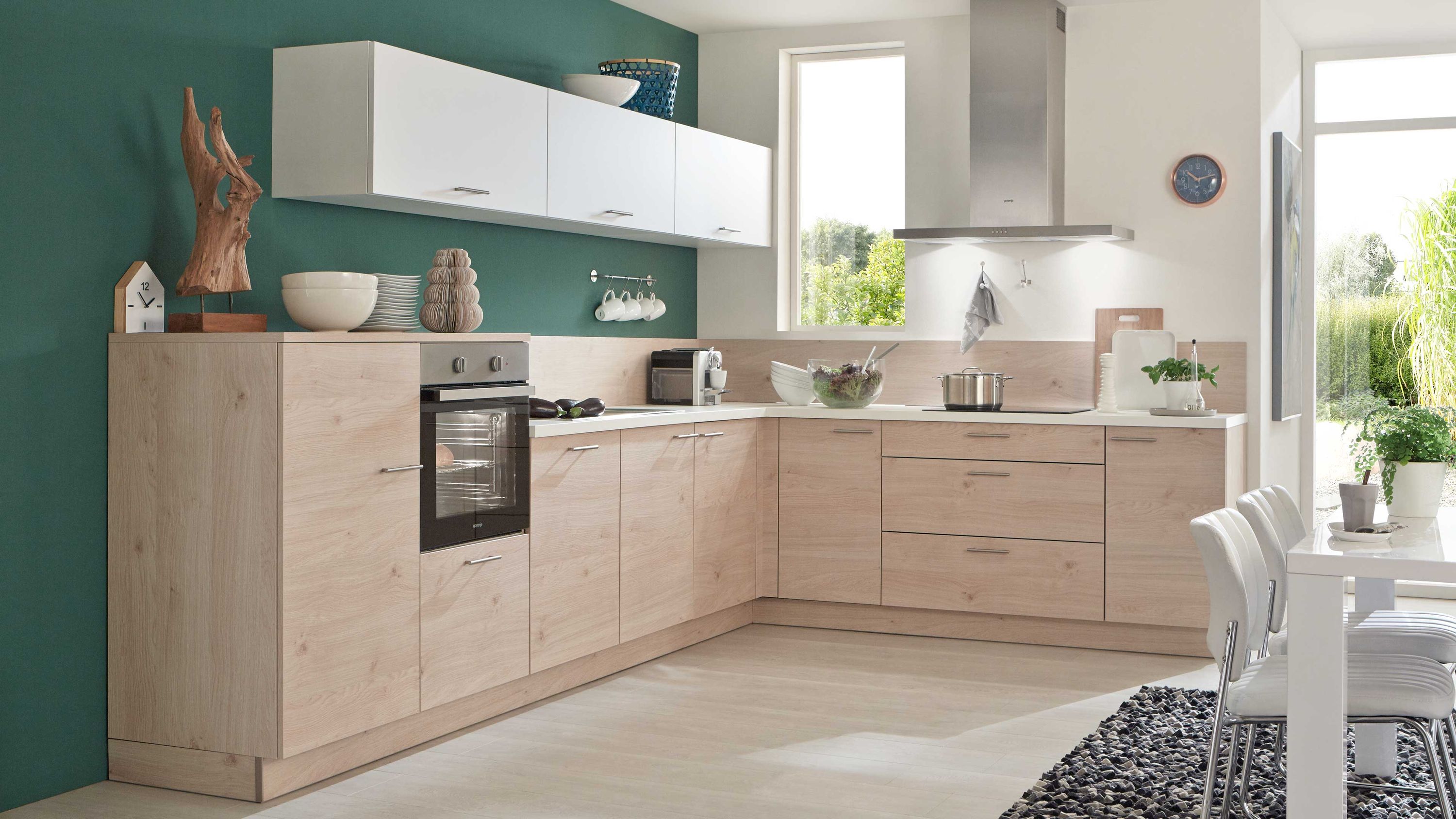 Küche mit grüner Akzentwand Holzfronten und heller Essecke Küche mit Holzschränken weißer Arbeitsplatte grüner Wand Einbauofen Esstisch mit weißen Stühlen