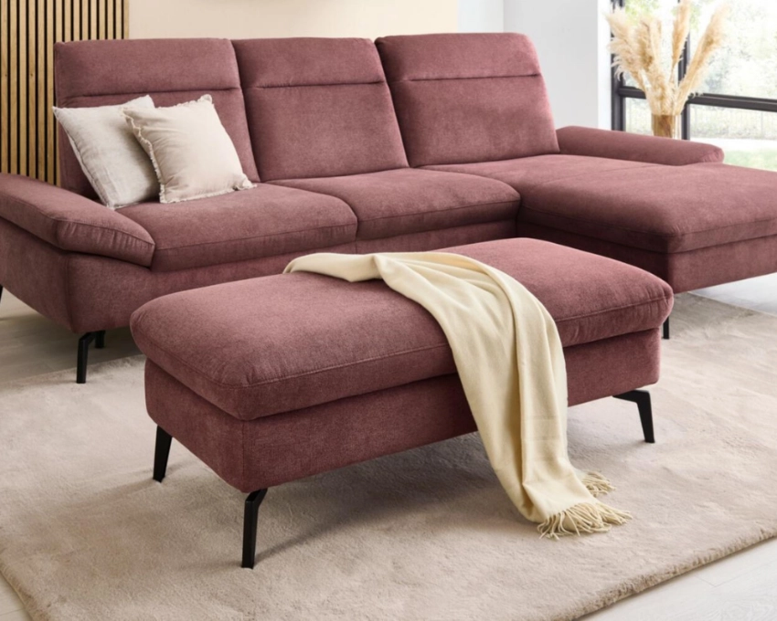 Modernes Ecksofa mit Relaxfunktion, stilvoll dekoriert in lichtdurchflutetem Wohnzimmer mit Naturakzenten Rosa Ecksofa mit Kopfstützen, Zierkissen und heller Decke auf Teppich vor Holzlamellenwand und Fenster