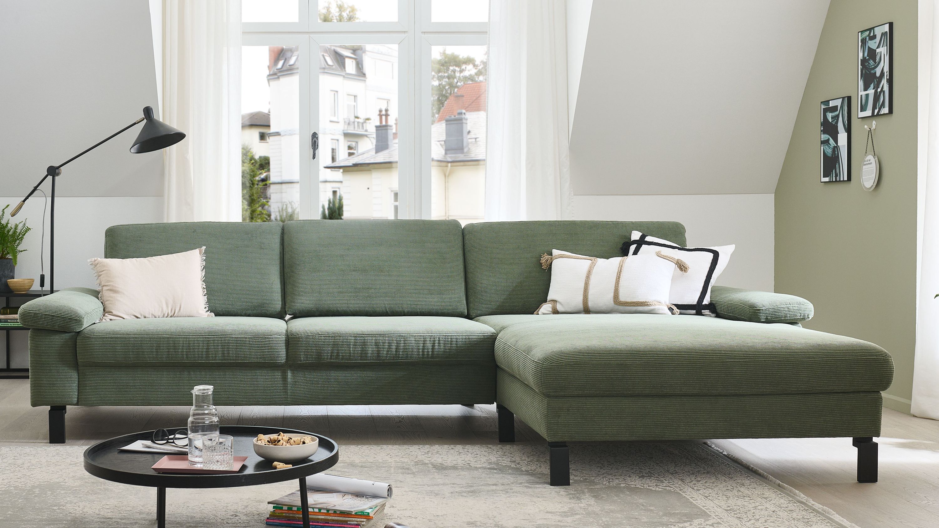 Ecksofa mit olivgrünem Feincordbezug und schwarzen Metallfüßen Ecksofa mit olivgrünem Feincordbezug und schwarzen Metallfüßen mit drei Rückenkissen und mehreren Zierkissen