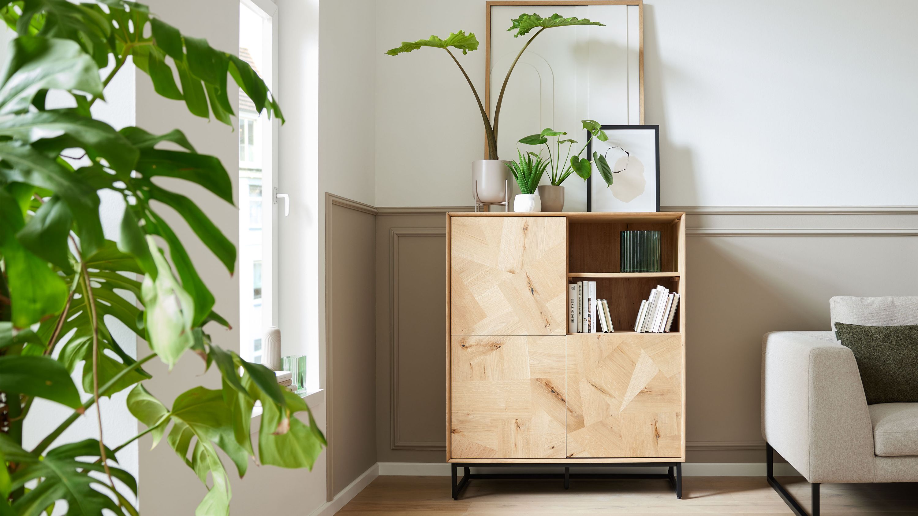 Helles Highboard mit vier Türen und zwei offenen Fächern Holzoptik schwarzes Metallgestell Pflanzen und Bilder darauf