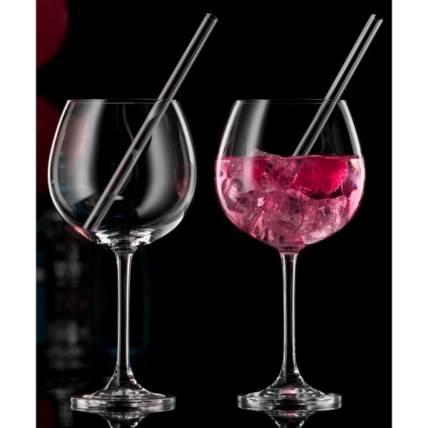Zwei Gingläser aus Kristall  eines leer  eines mit rosa Drink  Eiswürfeln und Strohhalm
