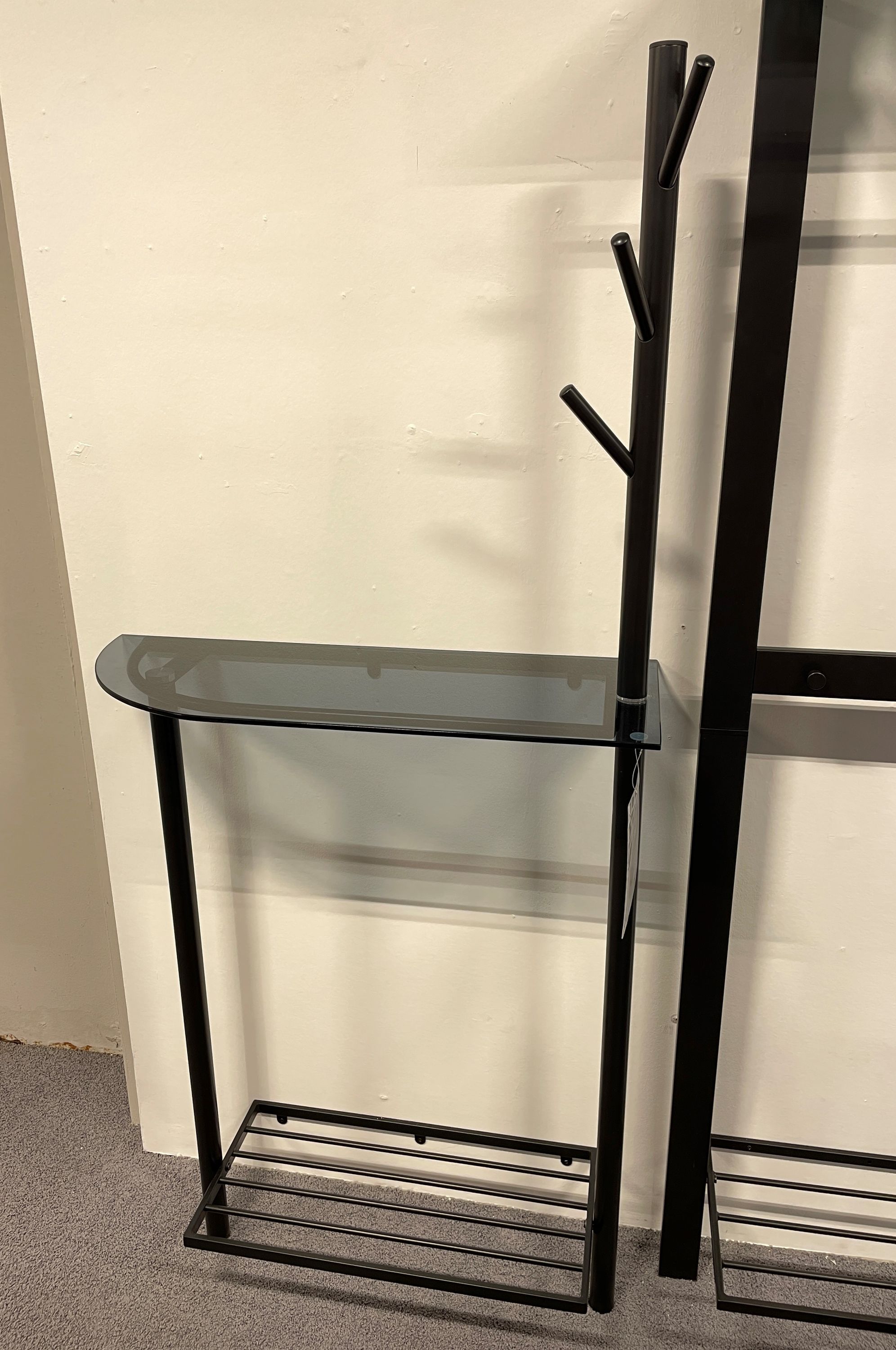 Schwarze Garderobe mit Glasablage Schlanke schwarze Garderobe mit Hakenstange, halbrunder Glasablage und unterem Ablagerost.