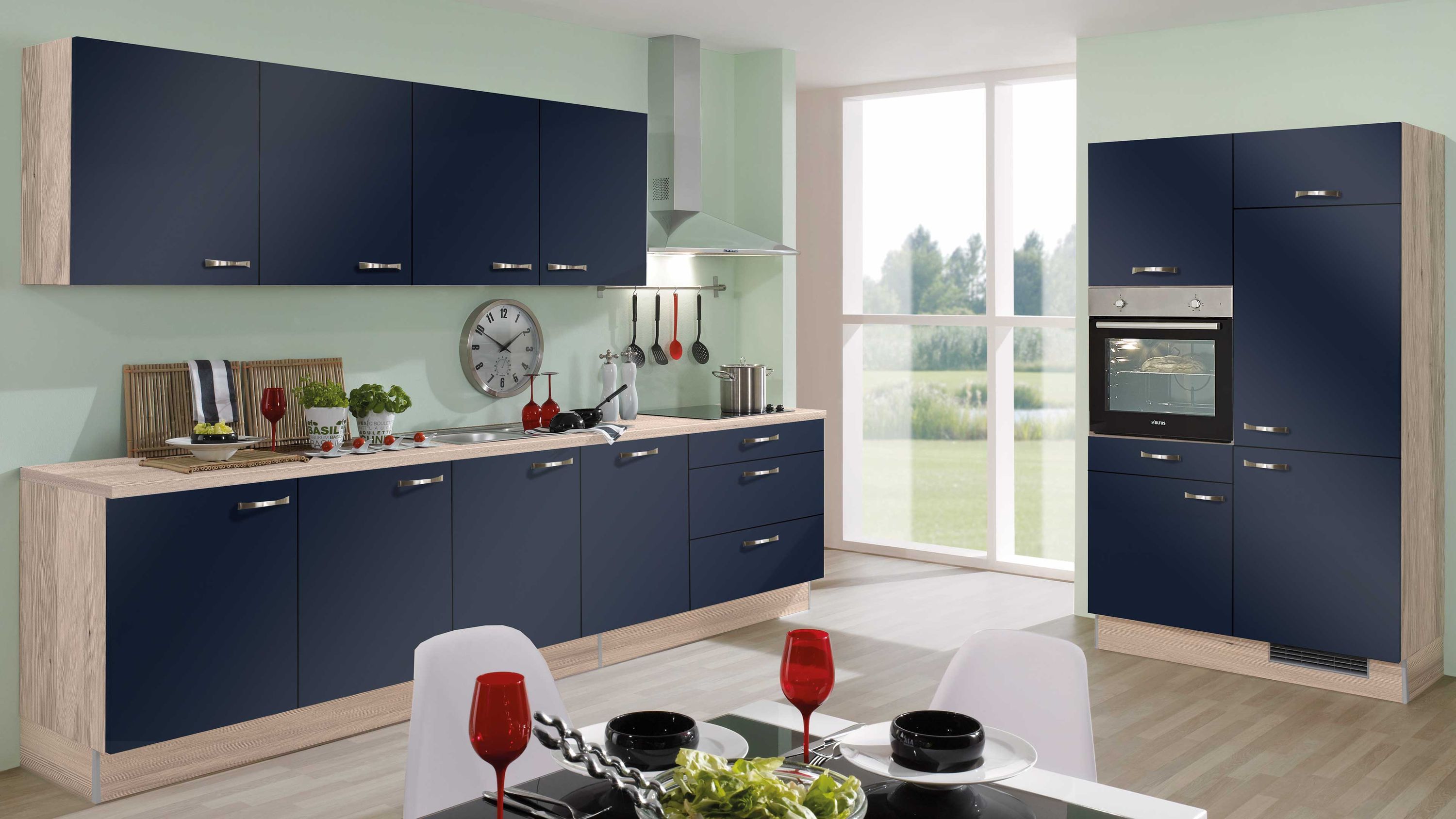 Küche in Navyblau mit gedecktem Tisch und Holzdetails Navyblaue Küche mit Holzakzenten Einbauofen Fensterlicht Esstisch mit Rotweingläsern schwarzen Tellern Deko.