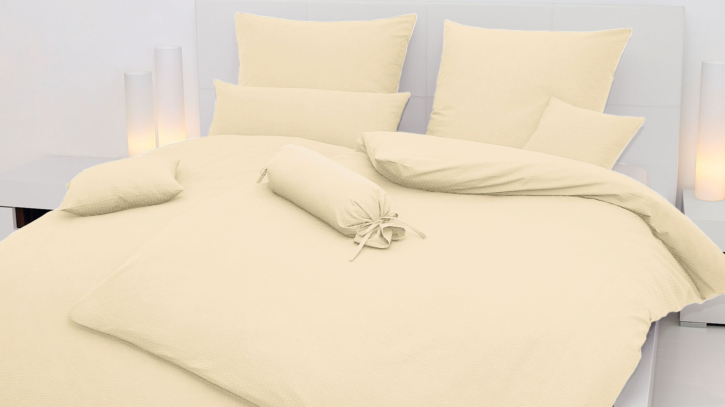 Bett mit cremefarbener Bettwäsche bestehend aus Kissen Zierkissen und Decke