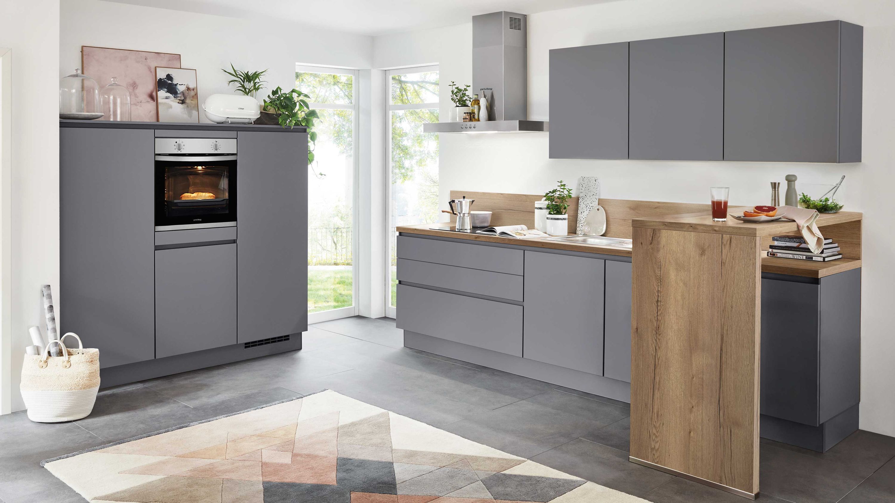 Graue Küche mit Holzplatte und geometrischem Teppich Graue Küche mit Holzarbeitsplatte Einbauofen Pflanzen Küchenutensilien Tageslicht geometrischer Teppich.