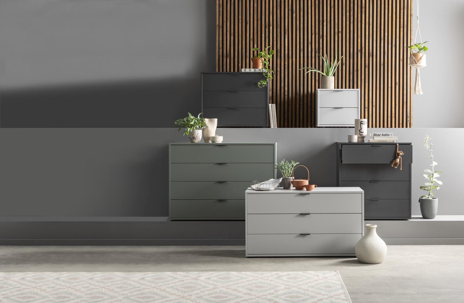 Stilvolle Kommoden in Grau und Grün vor Holzpaneel  modernes Arrangement mit Deko für zeitgemäßes Wohnen Mehrere moderne Kommoden in Grau- und Grüntönen vor Wand mit Holzpaneel  dekoriert mit Pflanzen und Vasen