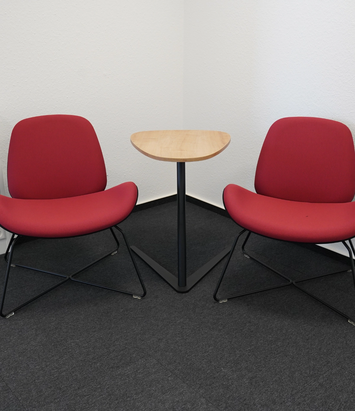 Zwei rote Loungesessel mit kleinem Beistelltisch, Teppichboden und minimalistischem Wartebereich im modernen Bürodesign