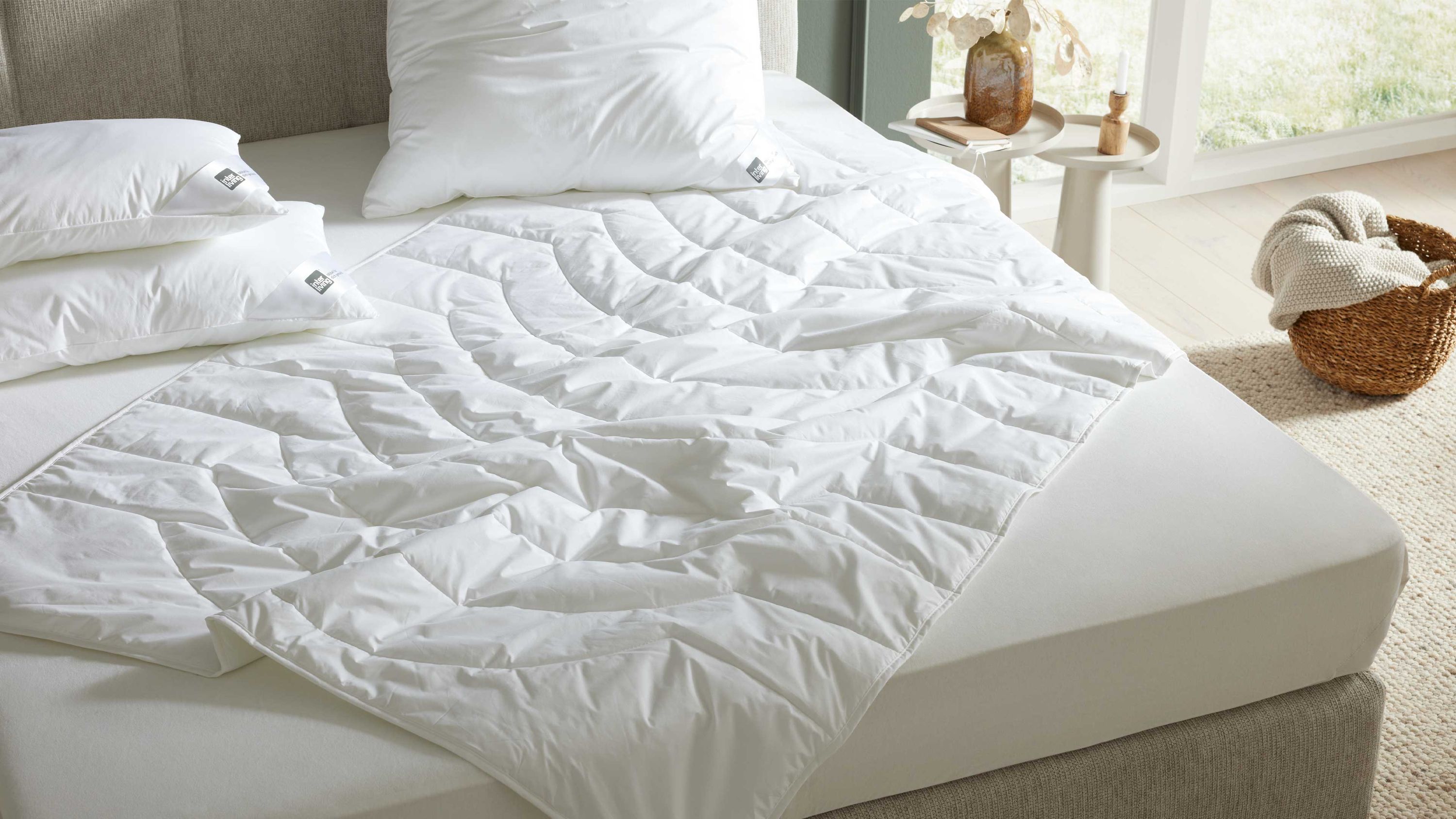 Weiße leichte Bettdecke mit gestepptem Muster auf einem Bett mit weißen Kissen