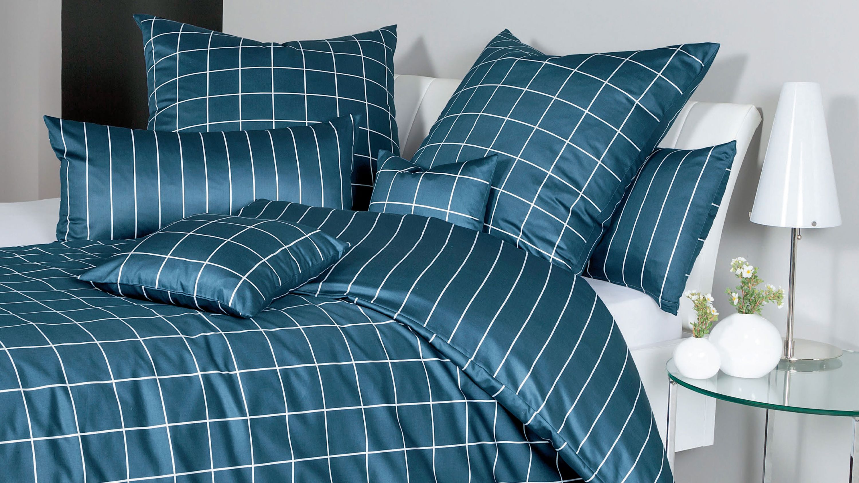 Bett mit dunkelblauer Bettwäsche mit weißen Karos und Streifen mehrere Kissen in verschiedenen Größen