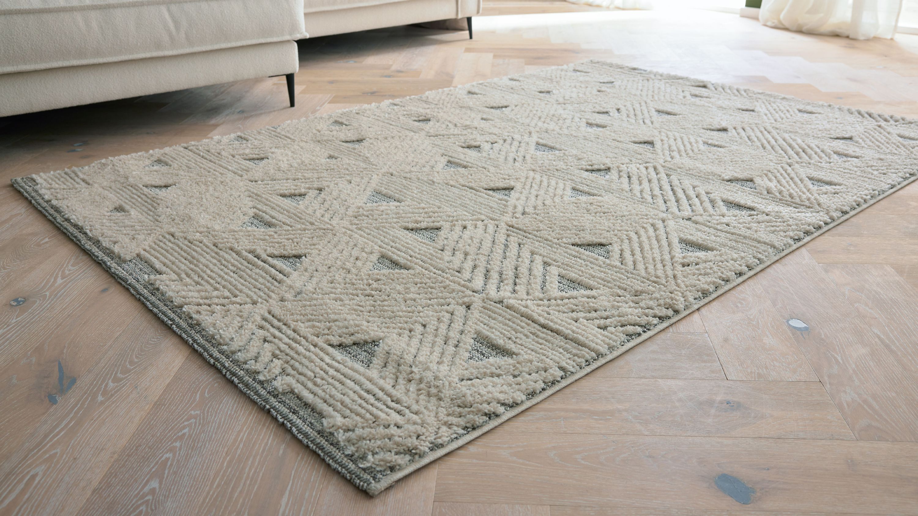 Rechteckiger Teppich mit geometrischem Muster in creme und grau auf hellem Holzboden