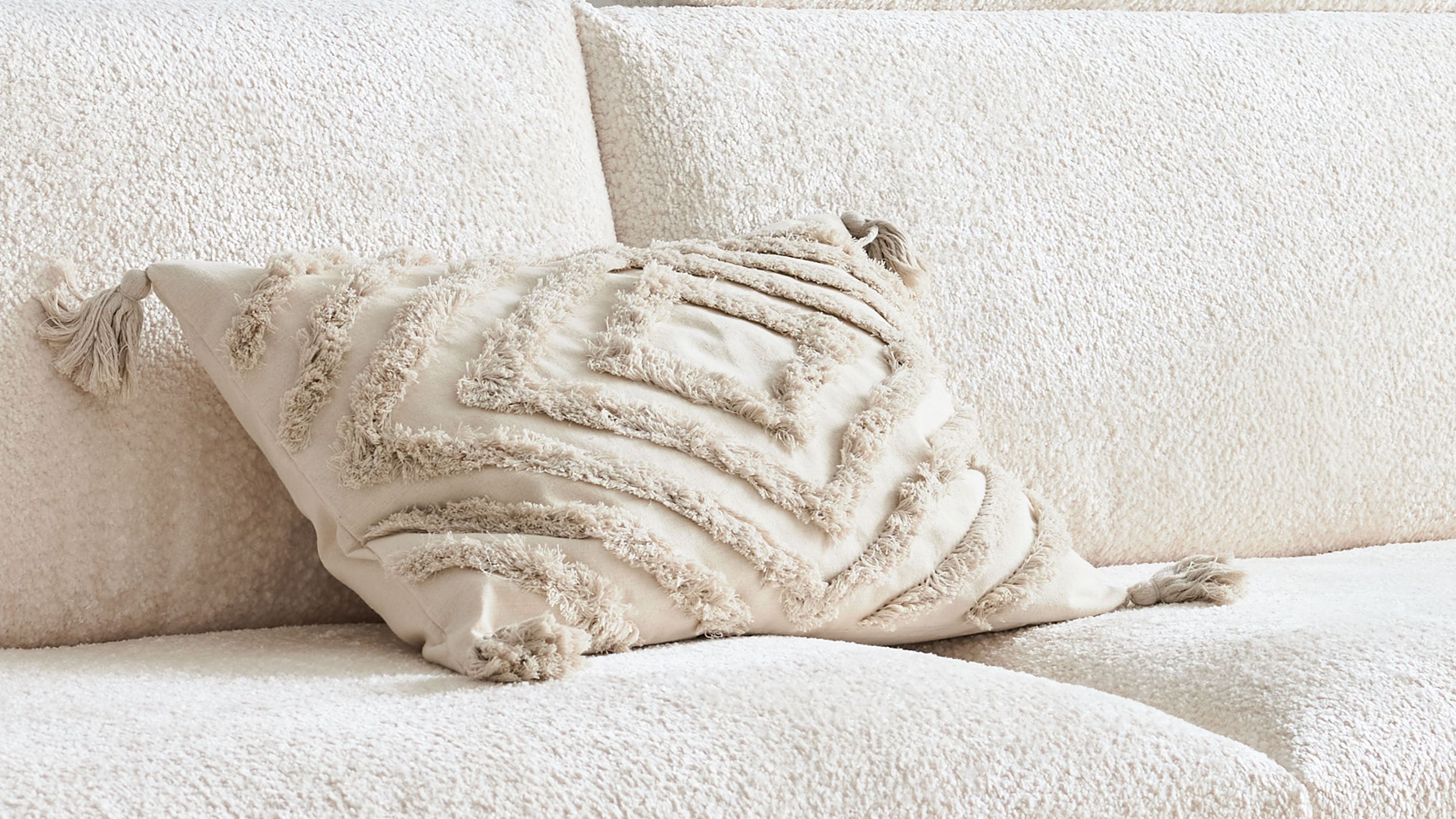 Beige Kissenhülle mit geometrischem Muster und Fransen an den Ecken auf hellem Sofa