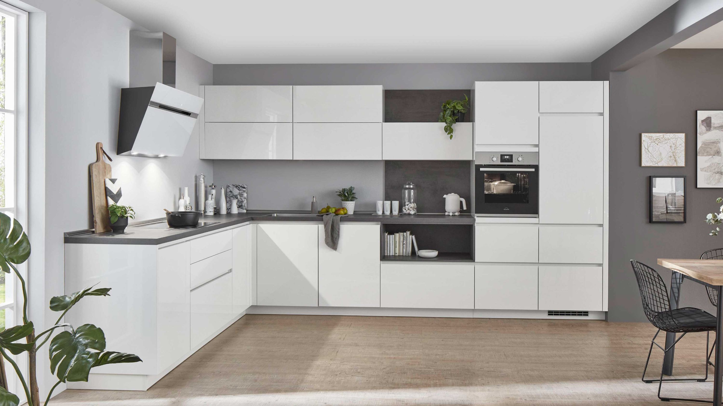 Glänzende L-Küche in Weiß mit grifflosen Fronten dunkler Arbeitsplatte Einbauofen und moderner Dunstabzugshaube.