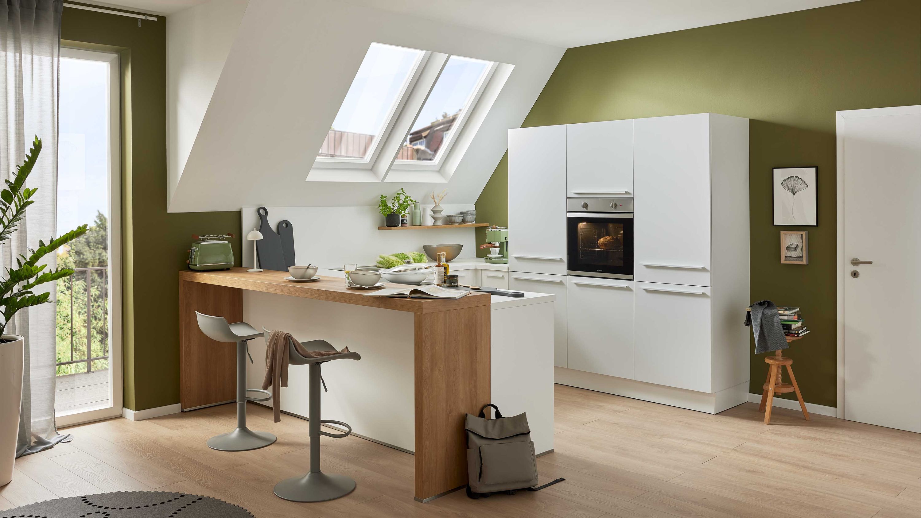 Weiße Küche mit Holztheke Einbauofen Dachfenstern und grüner Akzentwand in heller Raumgestaltung.
