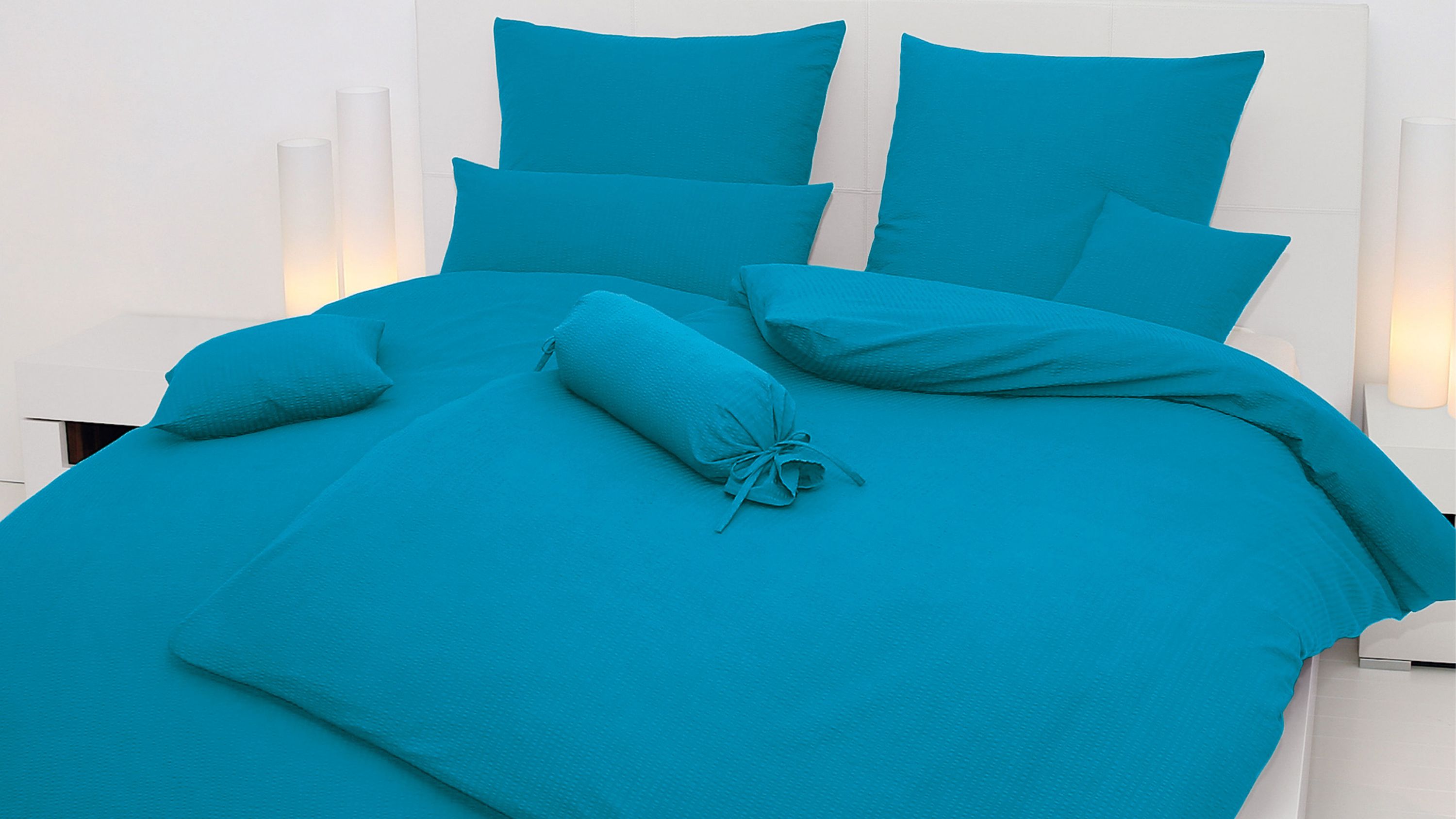 Bett mit einfarbiger blauer Bettwäsche bestehend aus Kissen Decke und Zierkissen