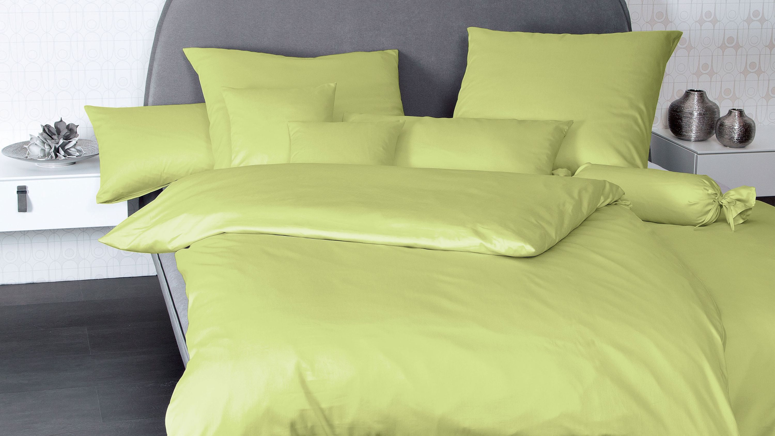 Bett mit apfelgrüner Bettwäsche bestehend aus Kissen und Decke auf grauem Kopfteil
