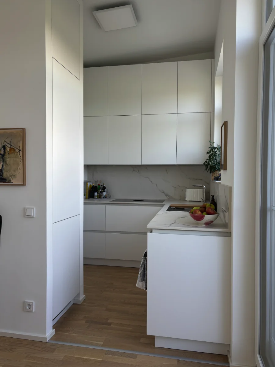 Kompakte weiße Küche mit Hochschränken, Holzarbeitsplatte, Spüle, Backofen und warmer Unterbauleuchtung.