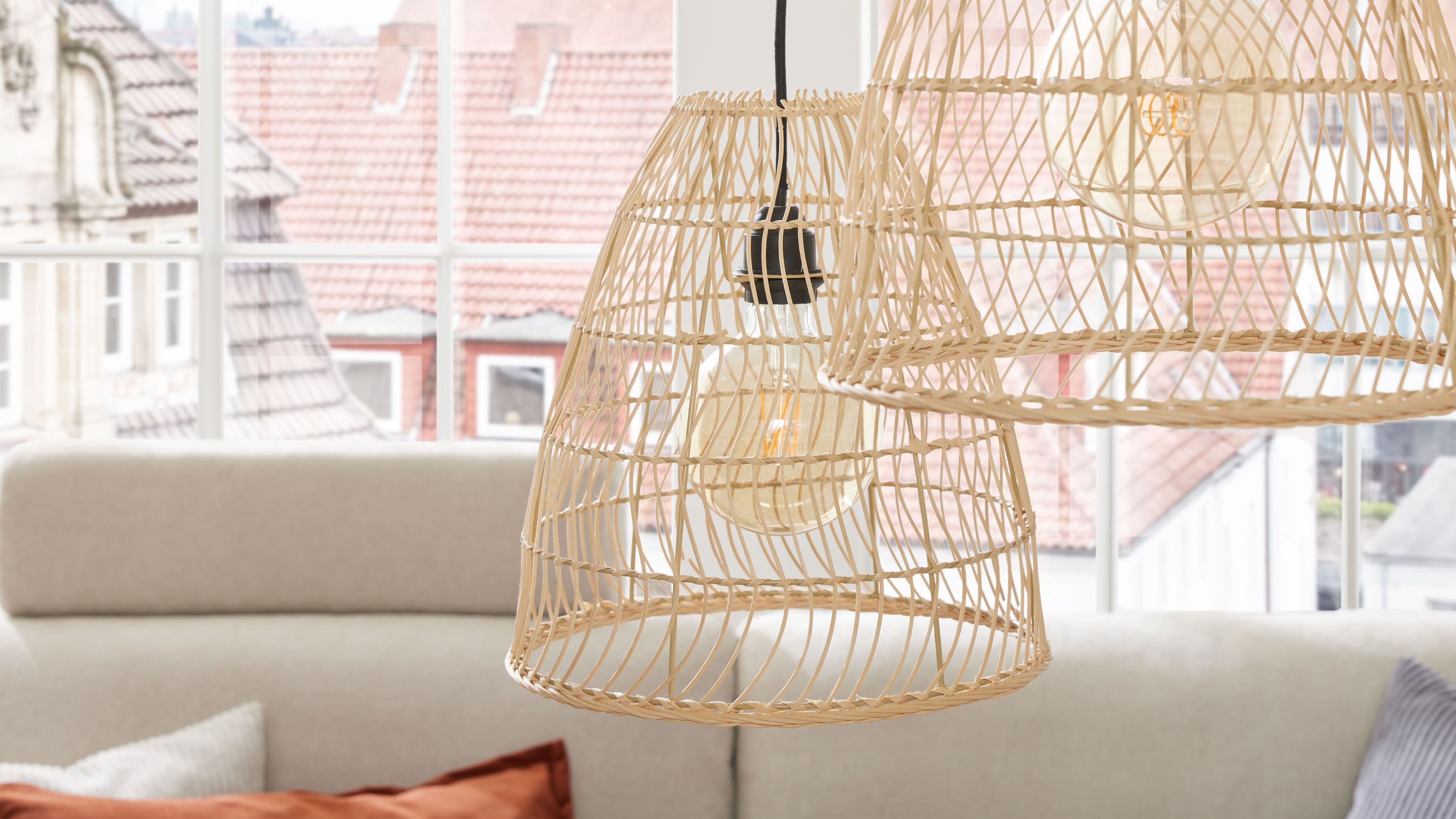 Runde Hängeleuchten aus Rattan mit schwarzer Fassung Zwei runde Hängeleuchten mit Rattangeflecht und schwarzer Fassung vor Fenster und Sofa