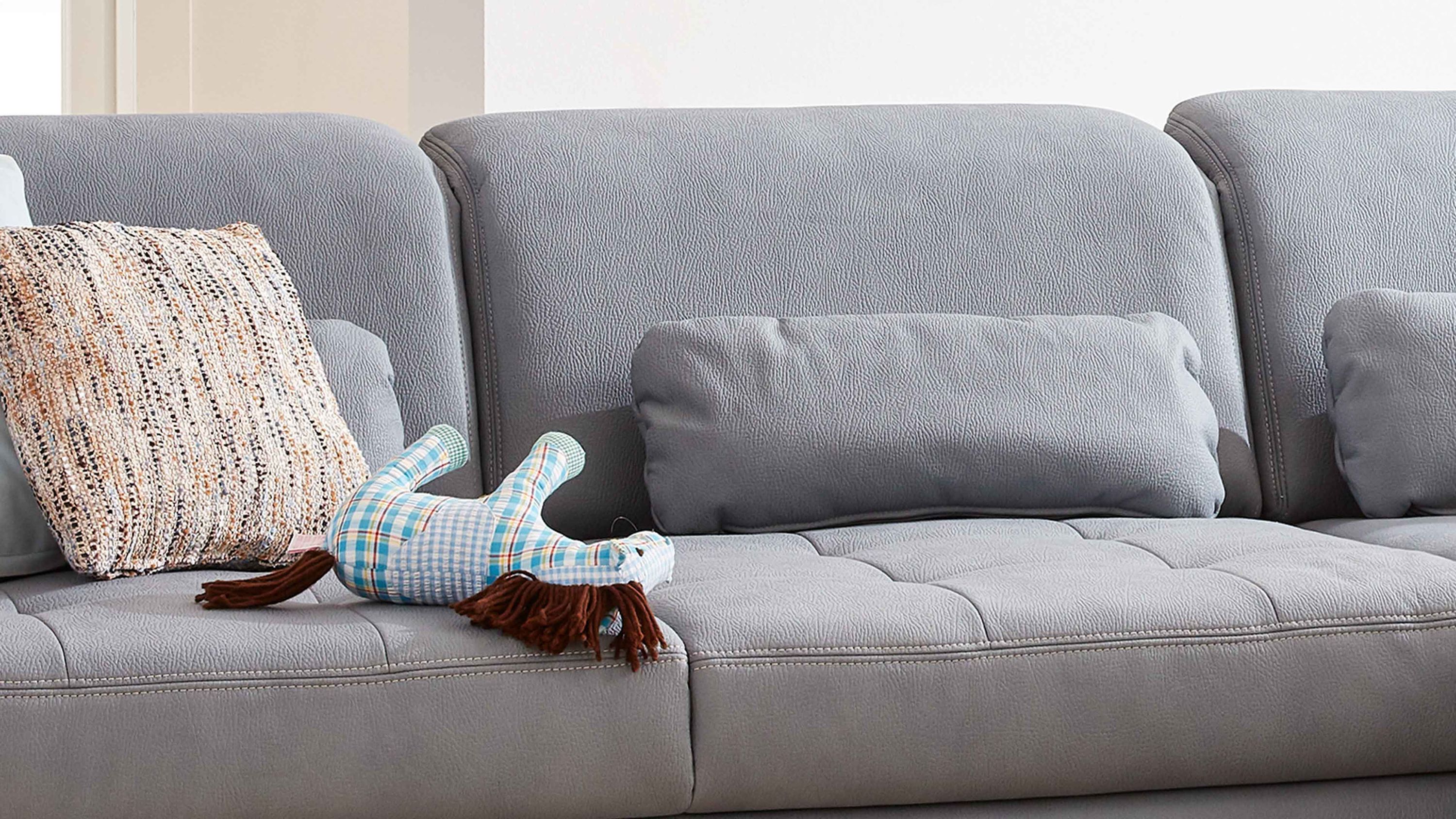 Graues Sofa mit gepolsterten Rückenlehnen und zwei grauen Nierenkissen aus Mikrofaser