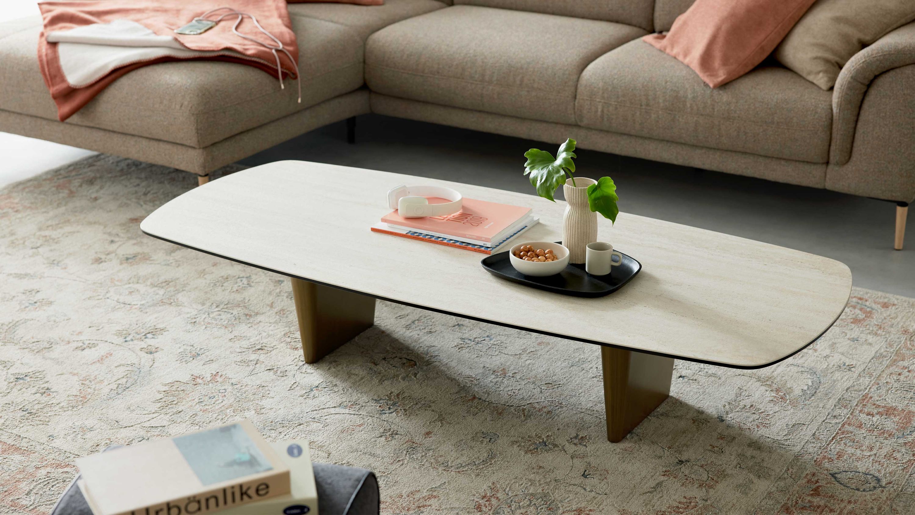 Couchtisch mit travertinfarbener Platte und bronzefarbenen Beinen Rechteckiger Couchtisch mit travertinfarbener Oberfläche und bronzefarbenen Beinen vor braunem Sofa