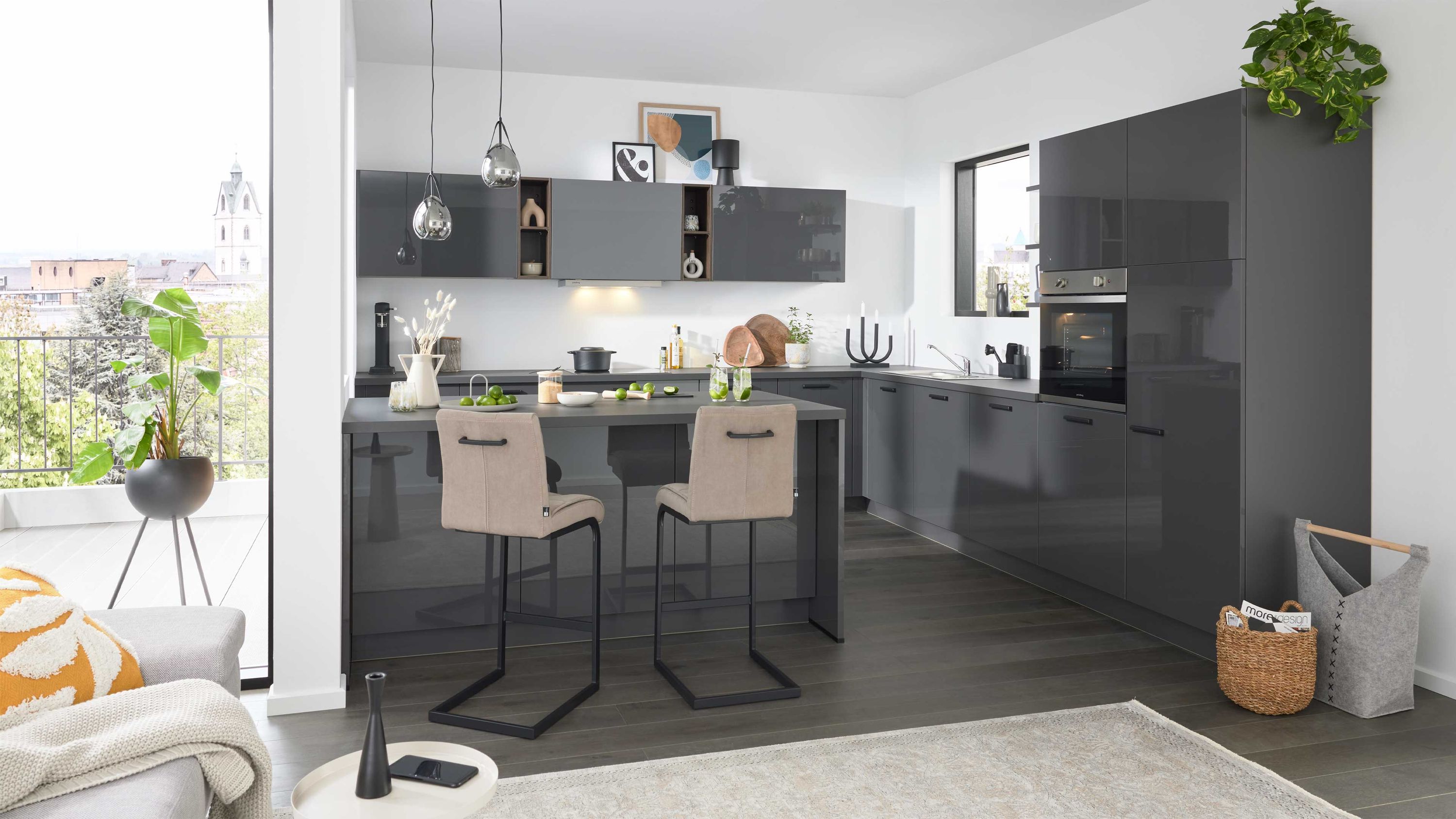 Dunkelgraue Schränke schwarze Inselplatte beige Barhocker dunkler Holzboden Fensterlicht Pflanzen und Küchenutensilien