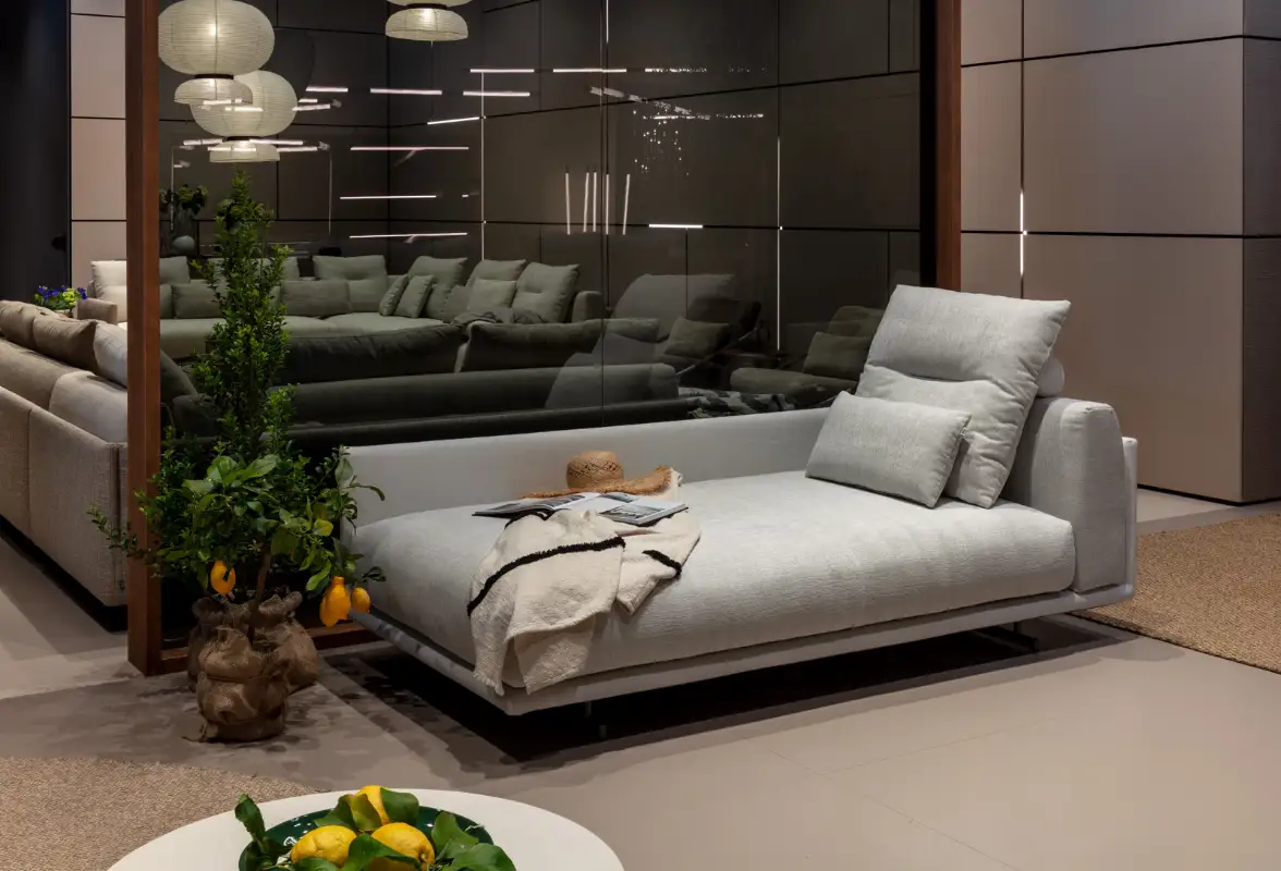 Elegante helle Recamiere mit verstellbarer Rückenlehne und Zierkissen, dekoriert mit einer Decke und Strohhut, vor einer modernen Spiegelwand im stilvollen Wohnbereich.