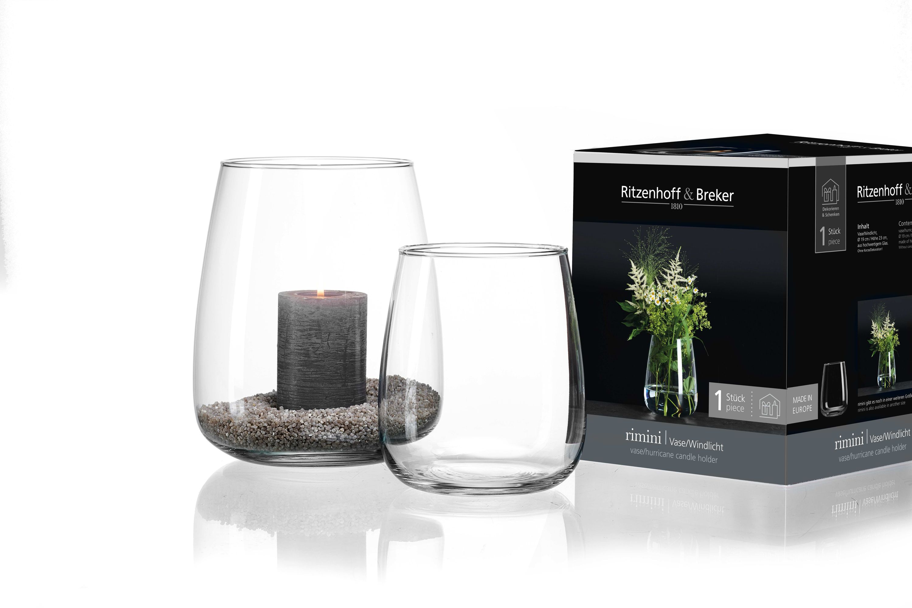 Zwei transparente Glasvasen mit abgerundeter Form eine mit grauer Kerze und Kieselsteinen gefüllt Verpackung mit Blumenmotiv