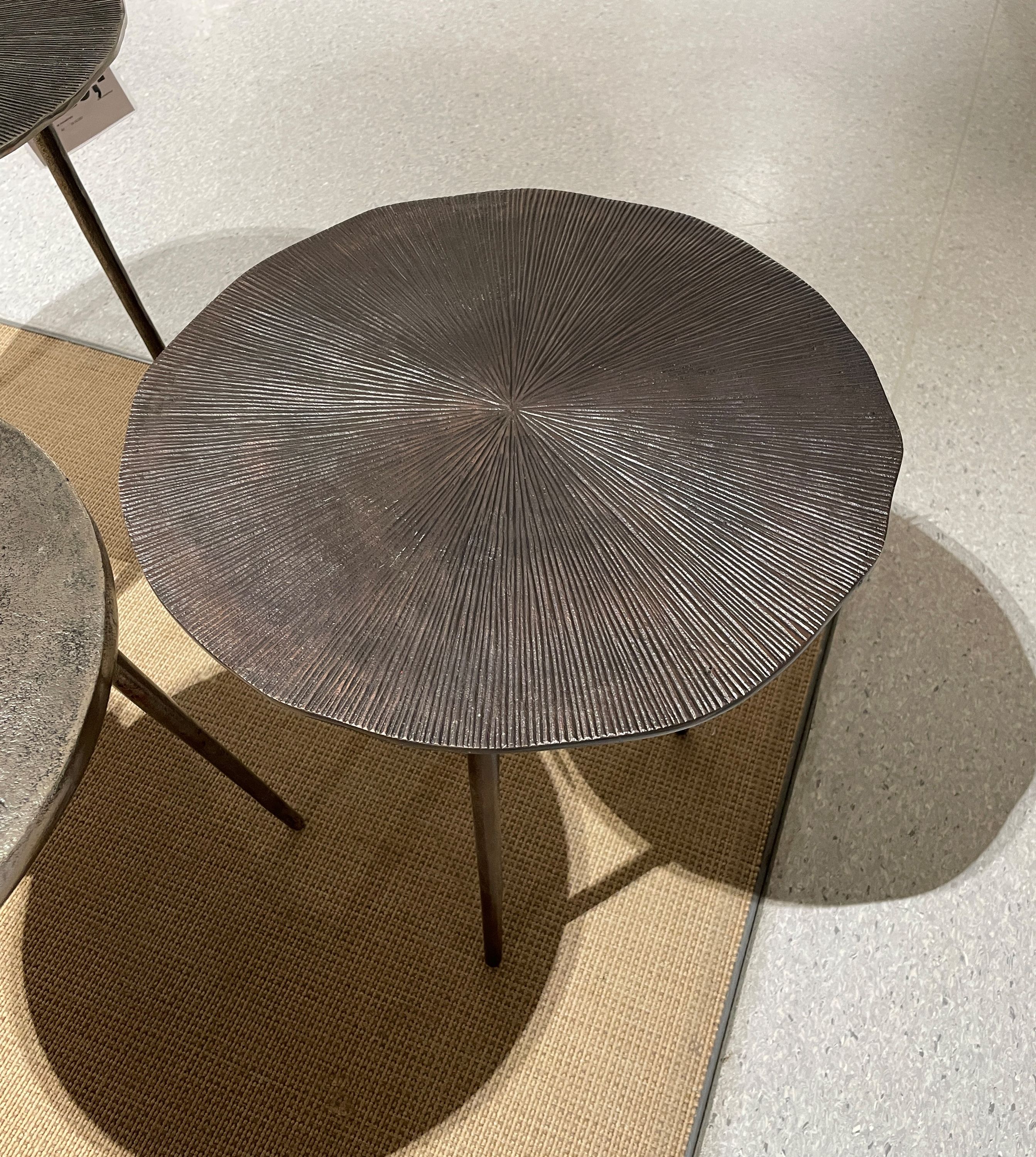 Runder Beistelltisch aus bronzefarbenem Metall mit radial strukturierter Oberfläche und drei schlanken Beinen.