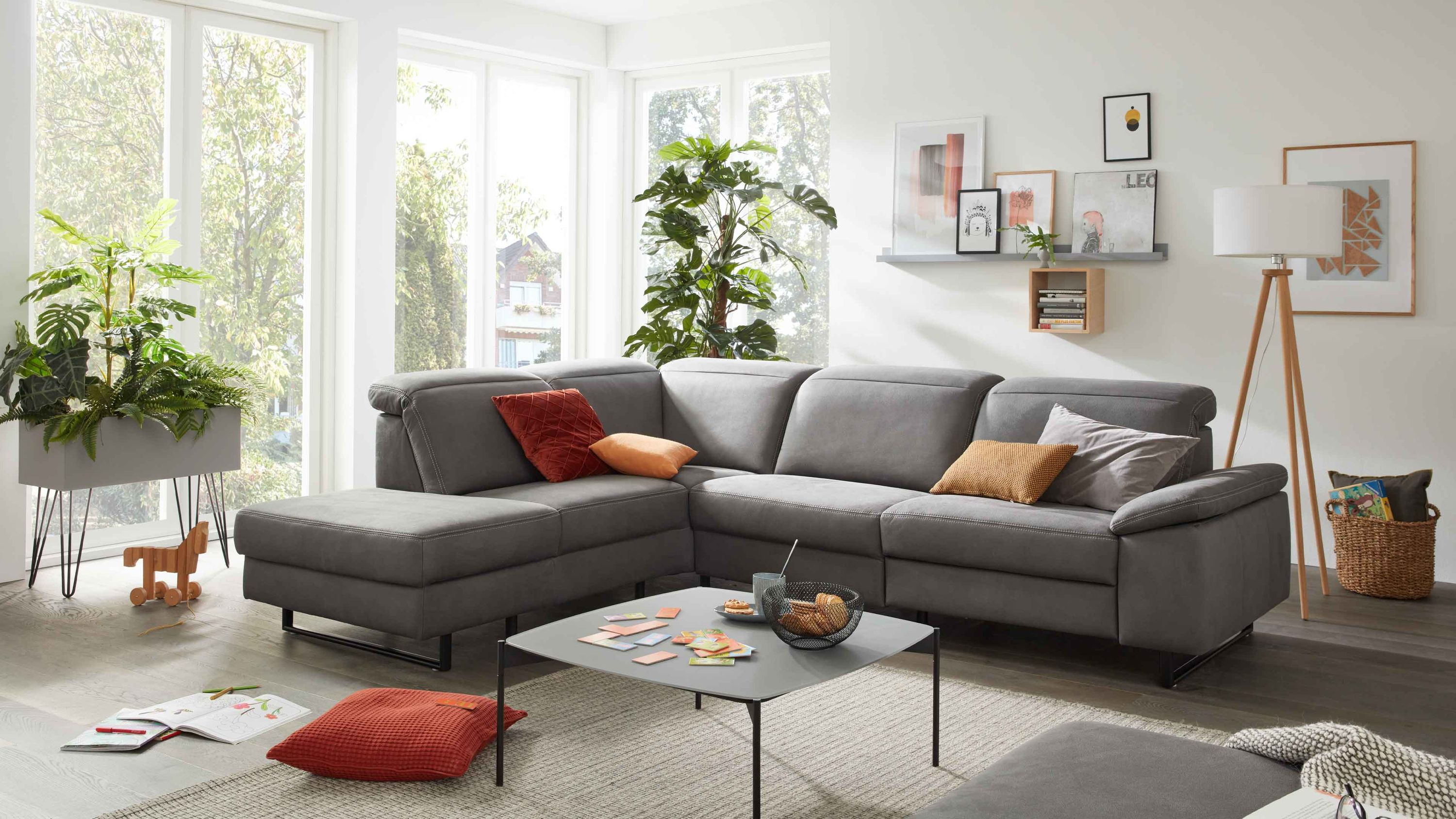 Ecksofa mit anthrazitfarbenem Stoffbezug und schwarzen Metallfüßen in hellem Wohnzimmer mit Kissen