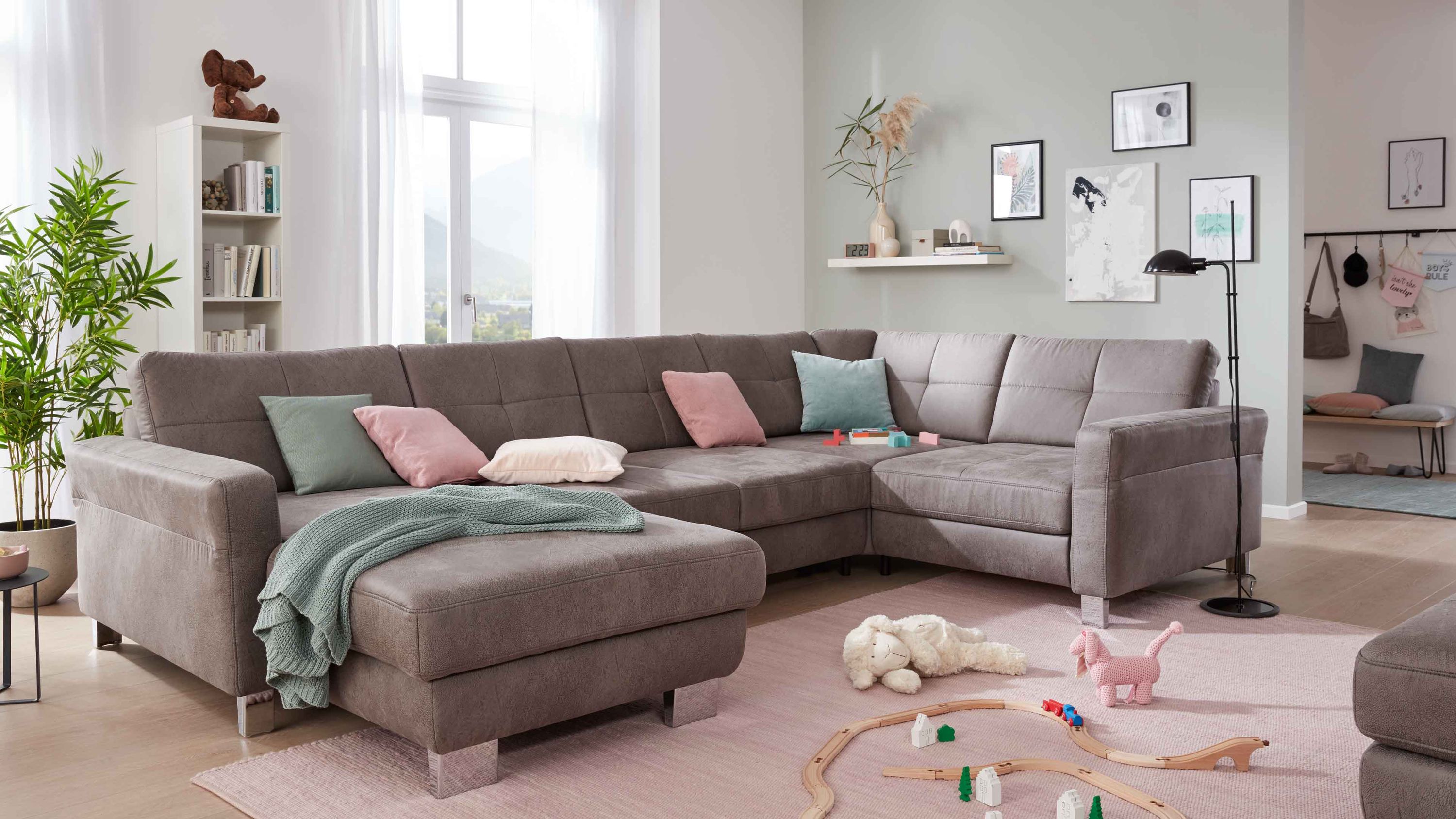 Ecksofa in grauer Mikrofaser mit Metallfüßen und mehreren bunten Kissen in einem hellen Wohnzimmer