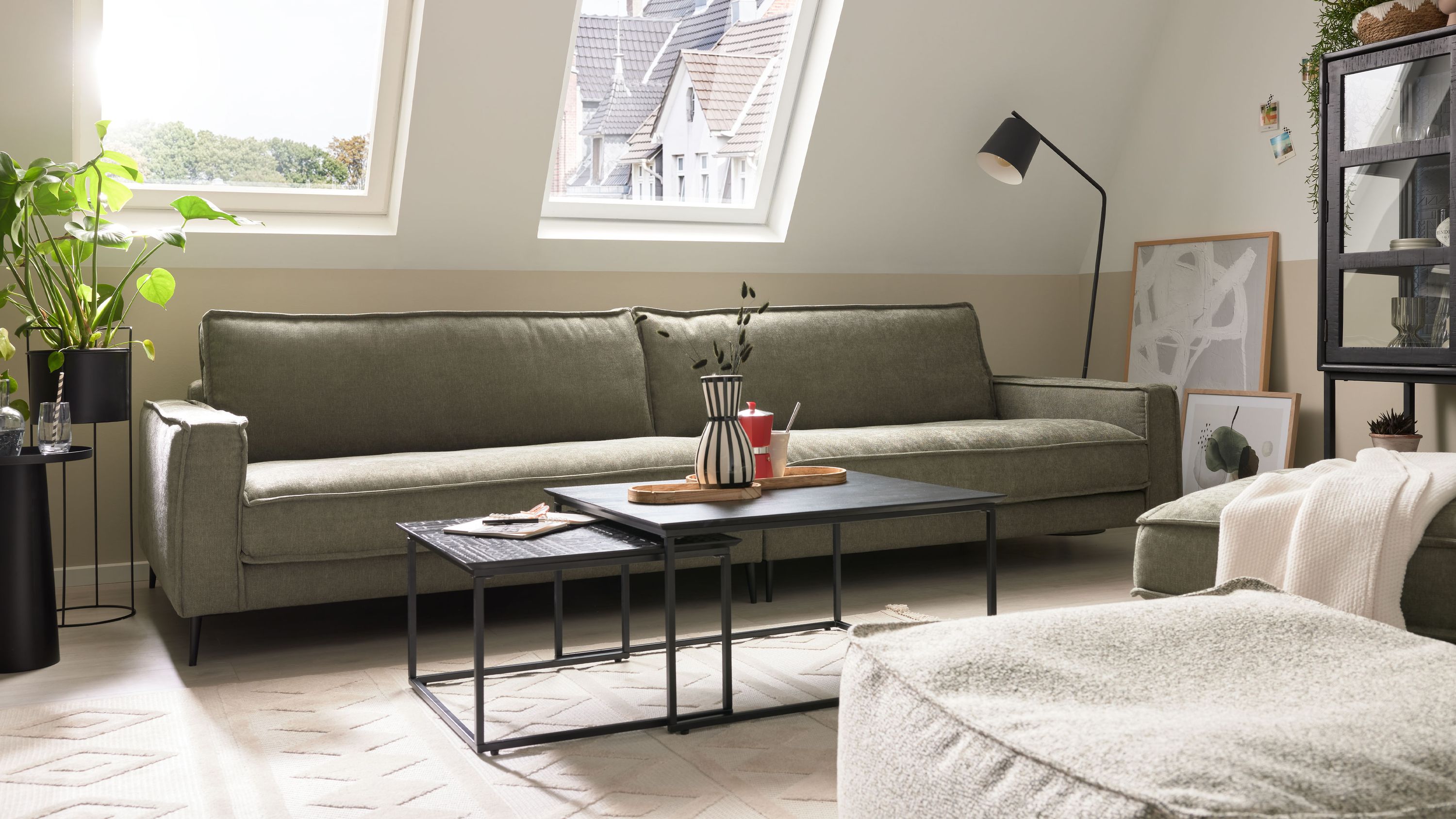 Großes grünes Sofa mit Metallfüßen Großes Sofa mit grünem Stoffbezug und Metallfüßen in einem hellen Wohnzimmer unter Dachfenstern
