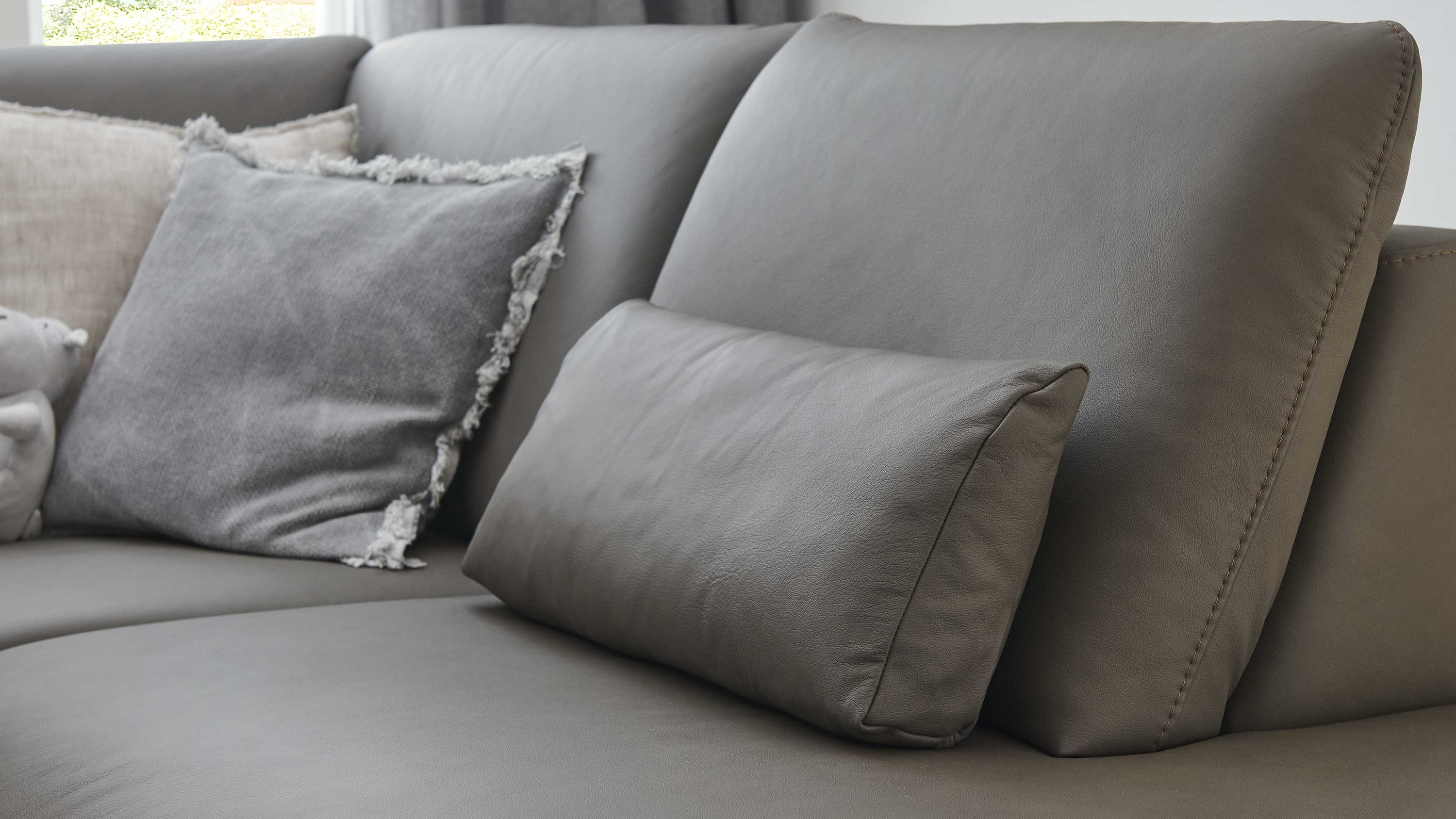 Rechteckiges Nierenkissen in steingrau auf grauem Sofa mit weiteren Kissen im Hintergrund