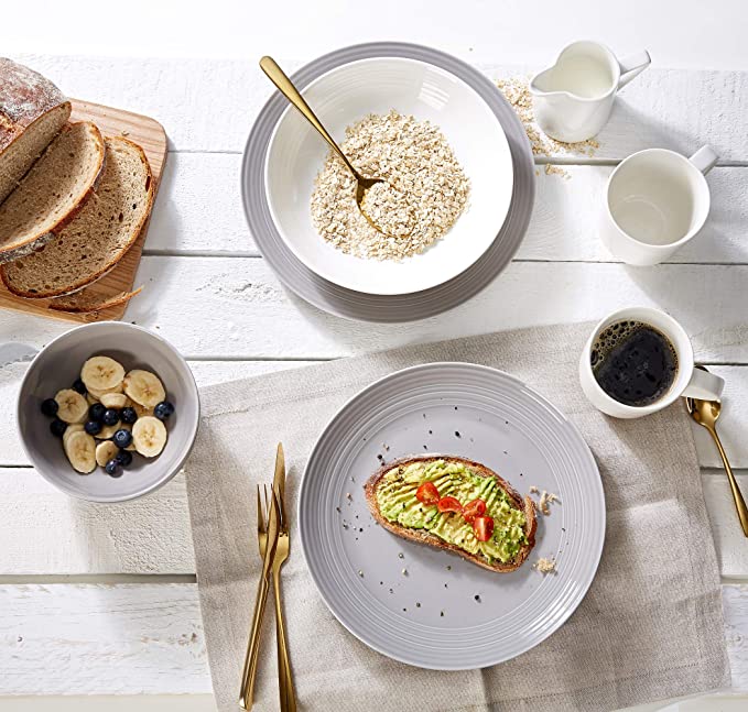 Vielfältiges Frühstück in Draufsicht Obere Draufsicht auf Frühstückstisch mit Haferflocken, Avocado-Toast, Obstschalen, Brotlaib und Kaffee.