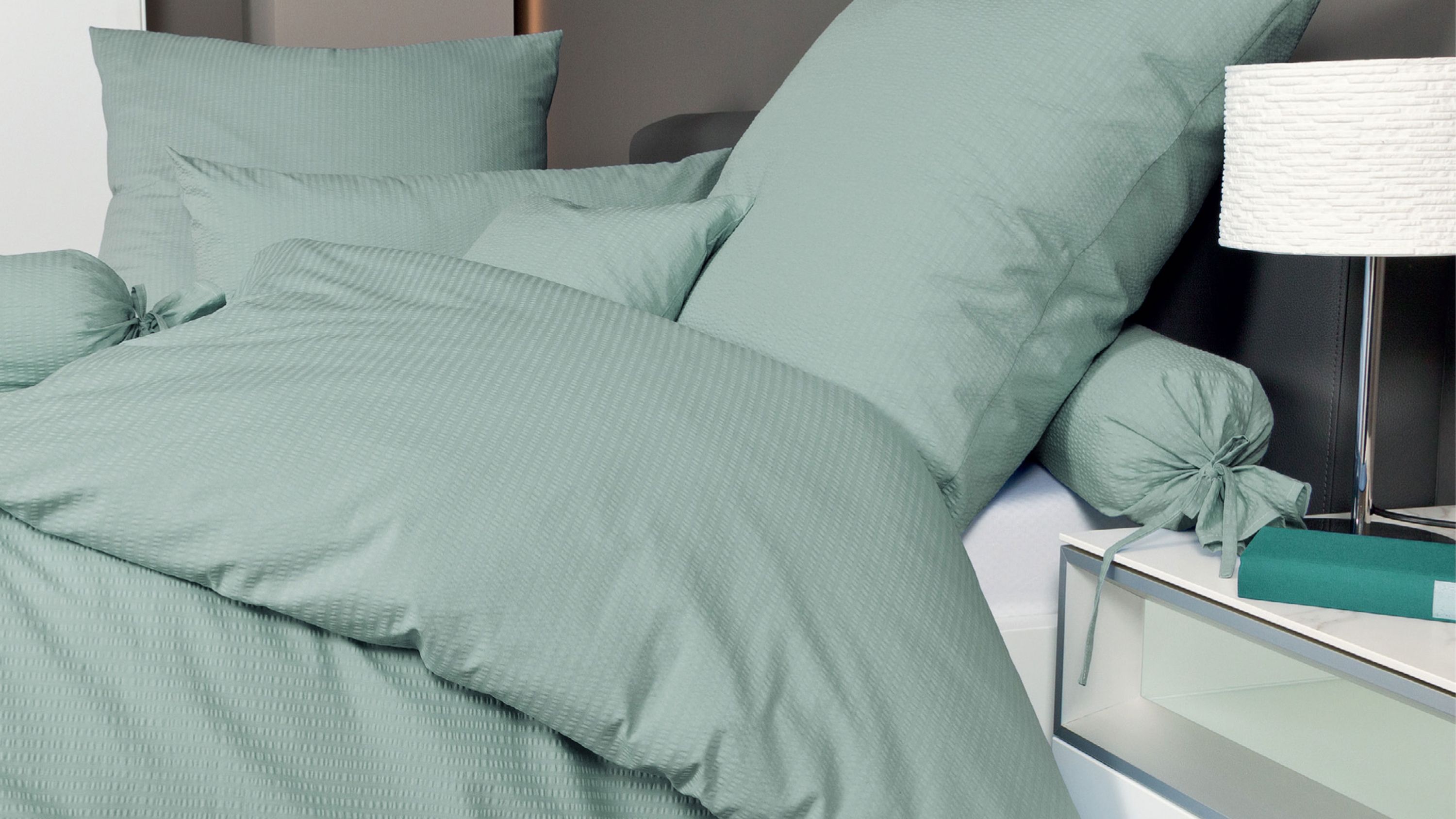 Bett mit rauchgrüner Bettwäsche bestehend aus Kissen und Decke mit feiner Struktur
