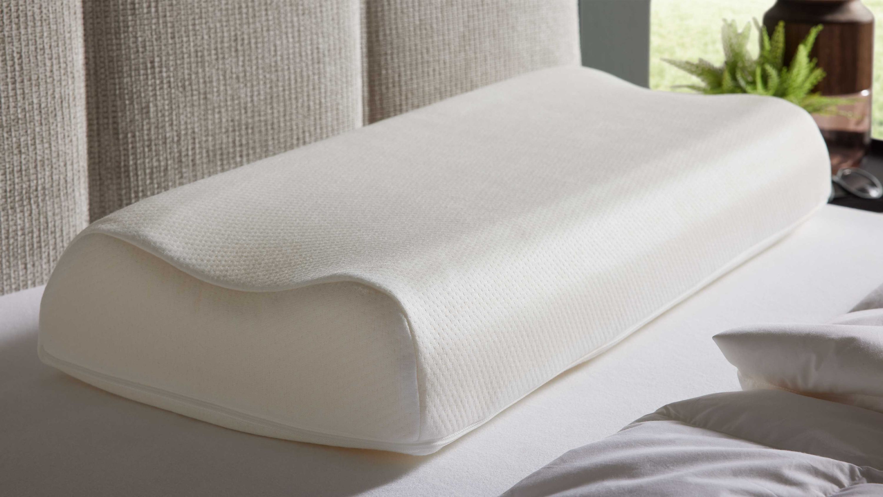 Weißes Nackenstützkissen mit ergonomischer Form auf weißer Matratze