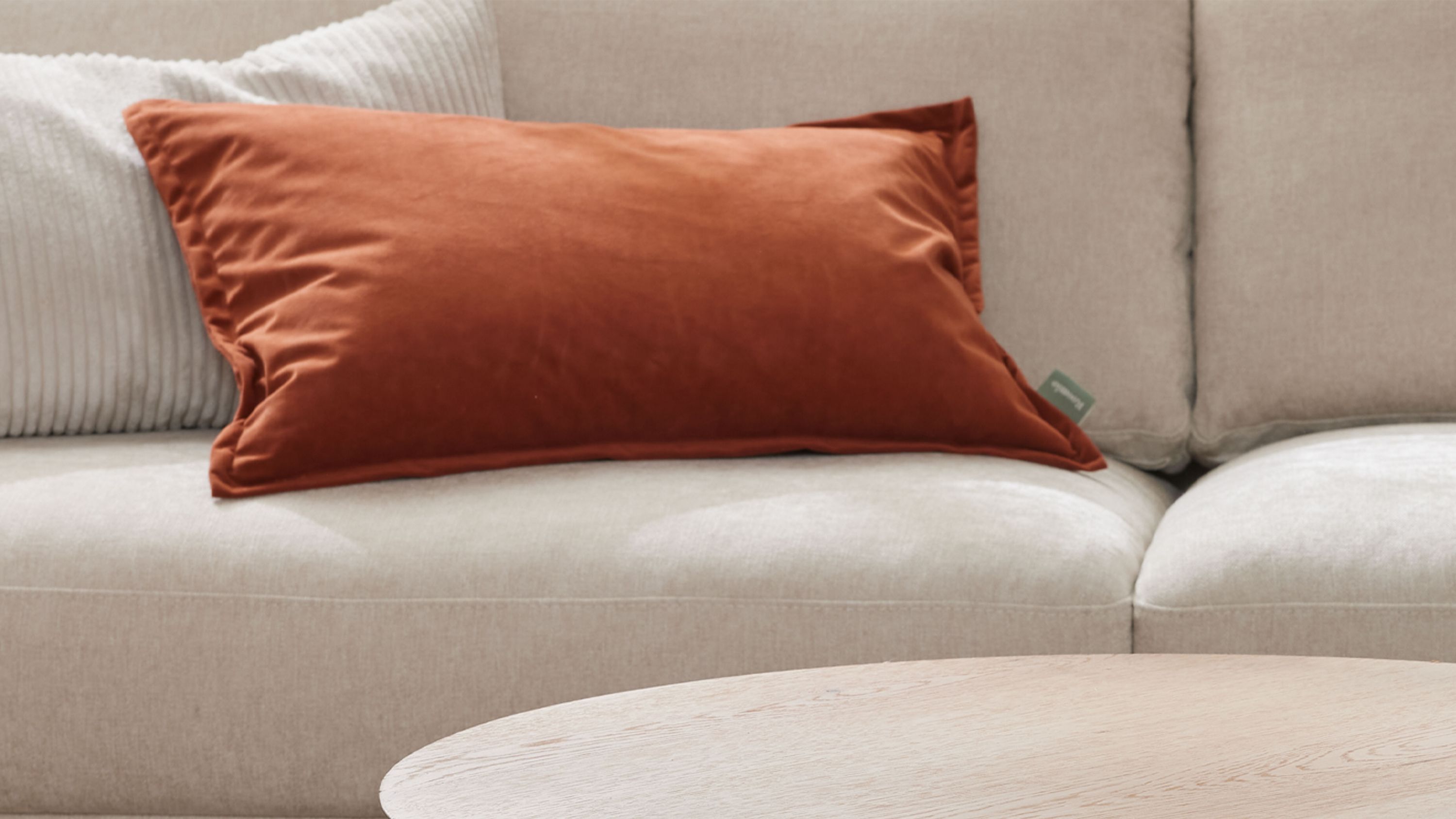 Rostfarbenes rechteckiges Kissen auf Sofa Rechteckiges rostfarbenes Kissen auf hellbeigem Sofa mit weiteren Kissen im Hintergrund