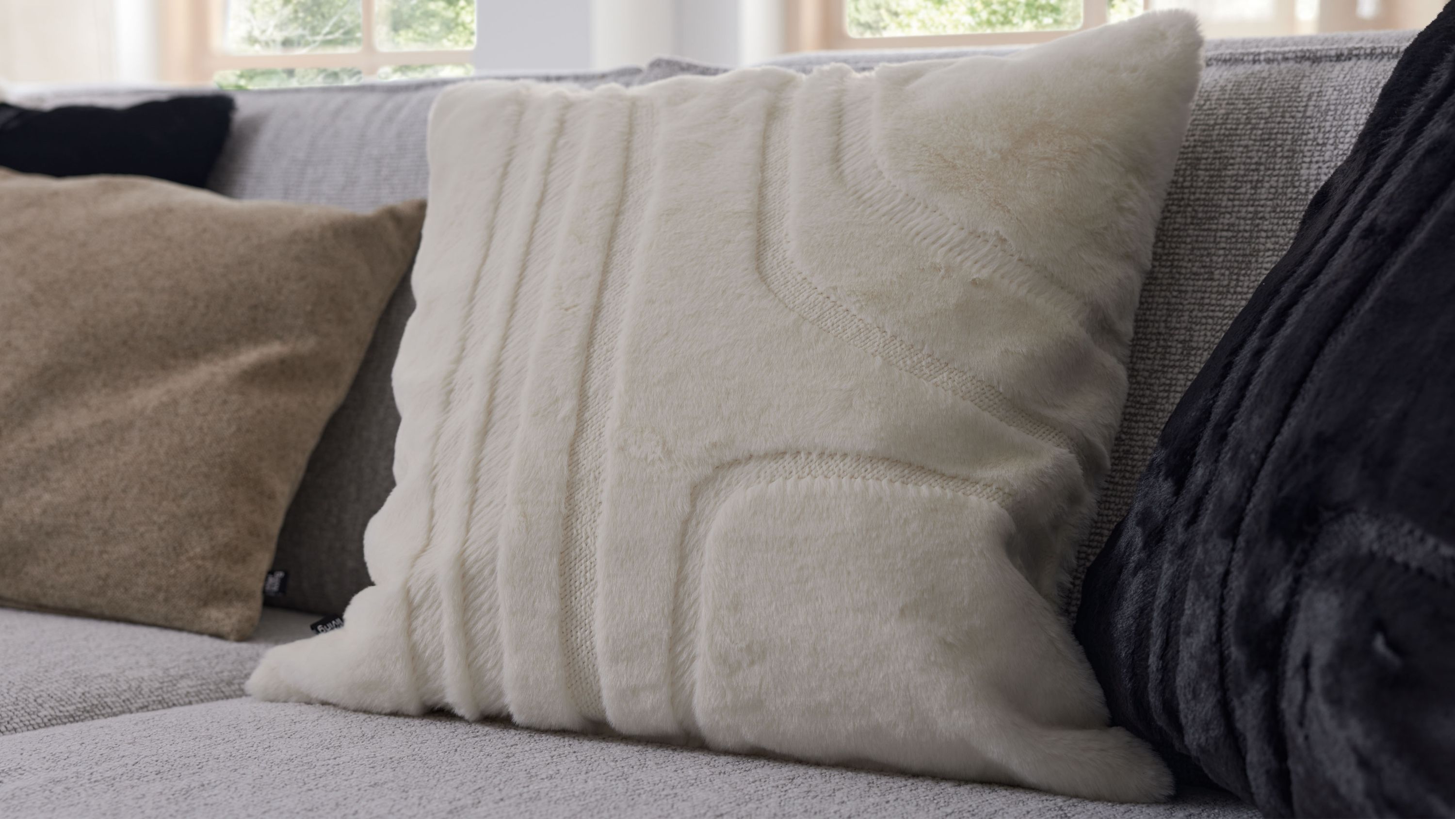 Quadratisches Kissen mit naturfarbener strukturierter Oberfläche aus Kunstfell auf grauem Sofa