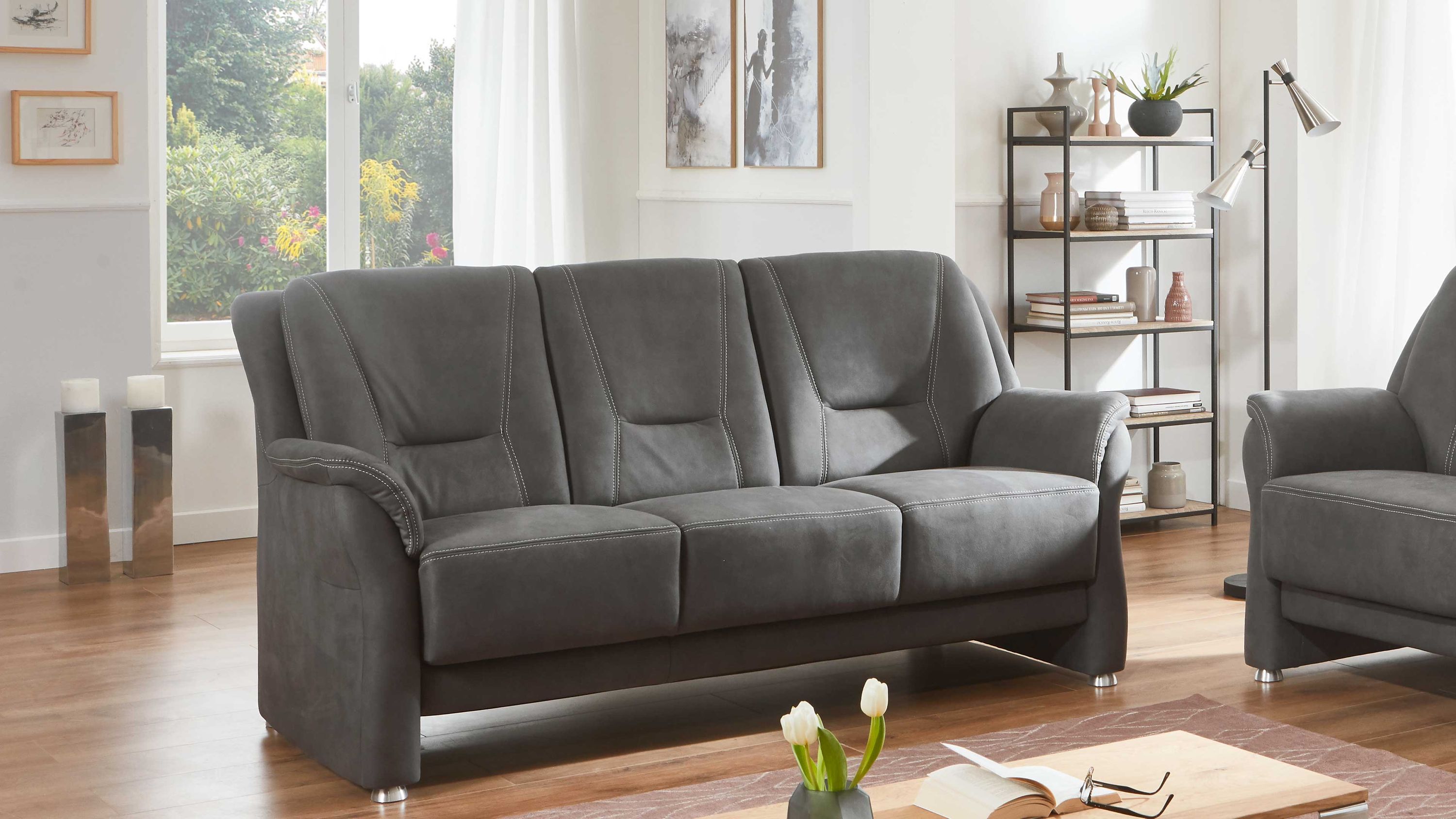 Dreisitziges graues Sofa mit gepolsterten Armlehnen und Metallfüßen in einem hellen Wohnzimmer