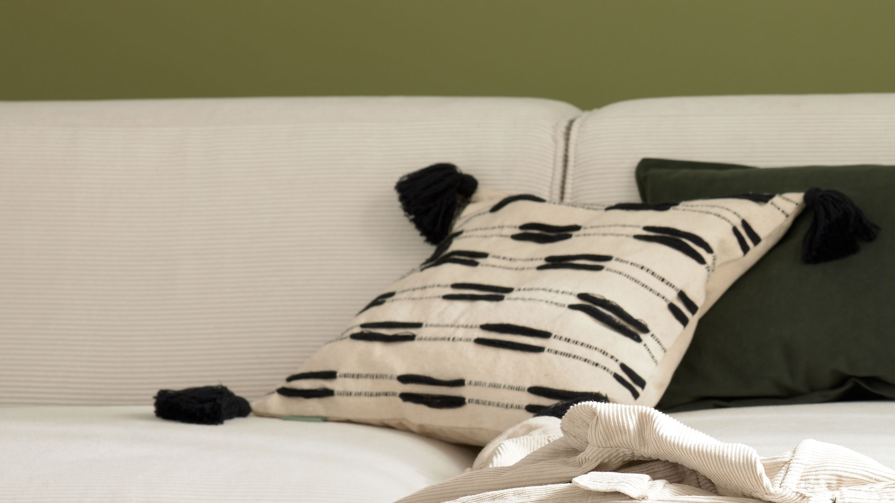 Beige Kissenhülle mit schwarzem Muster und Quasten Quadratische Kissenhülle mit schwarzen Mustern und Quasten auf beigem Hintergrund auf einem hellen Sofa