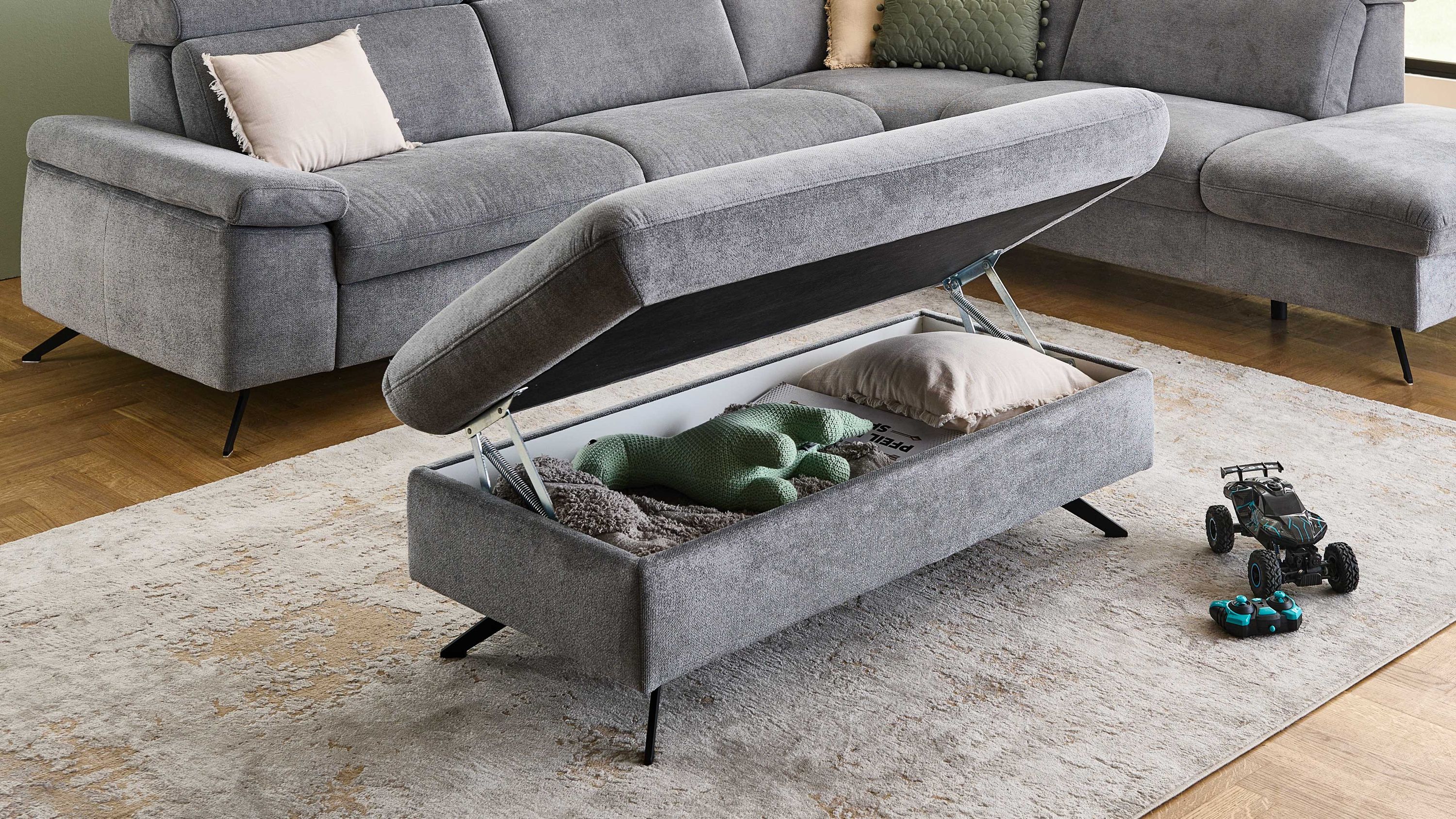 Grauer rechteckiger Hocker mit aufklappbarem Sitz und schwarzer Metallbeinen geöffnet mit Decke Kissen und Spielzeug darin
