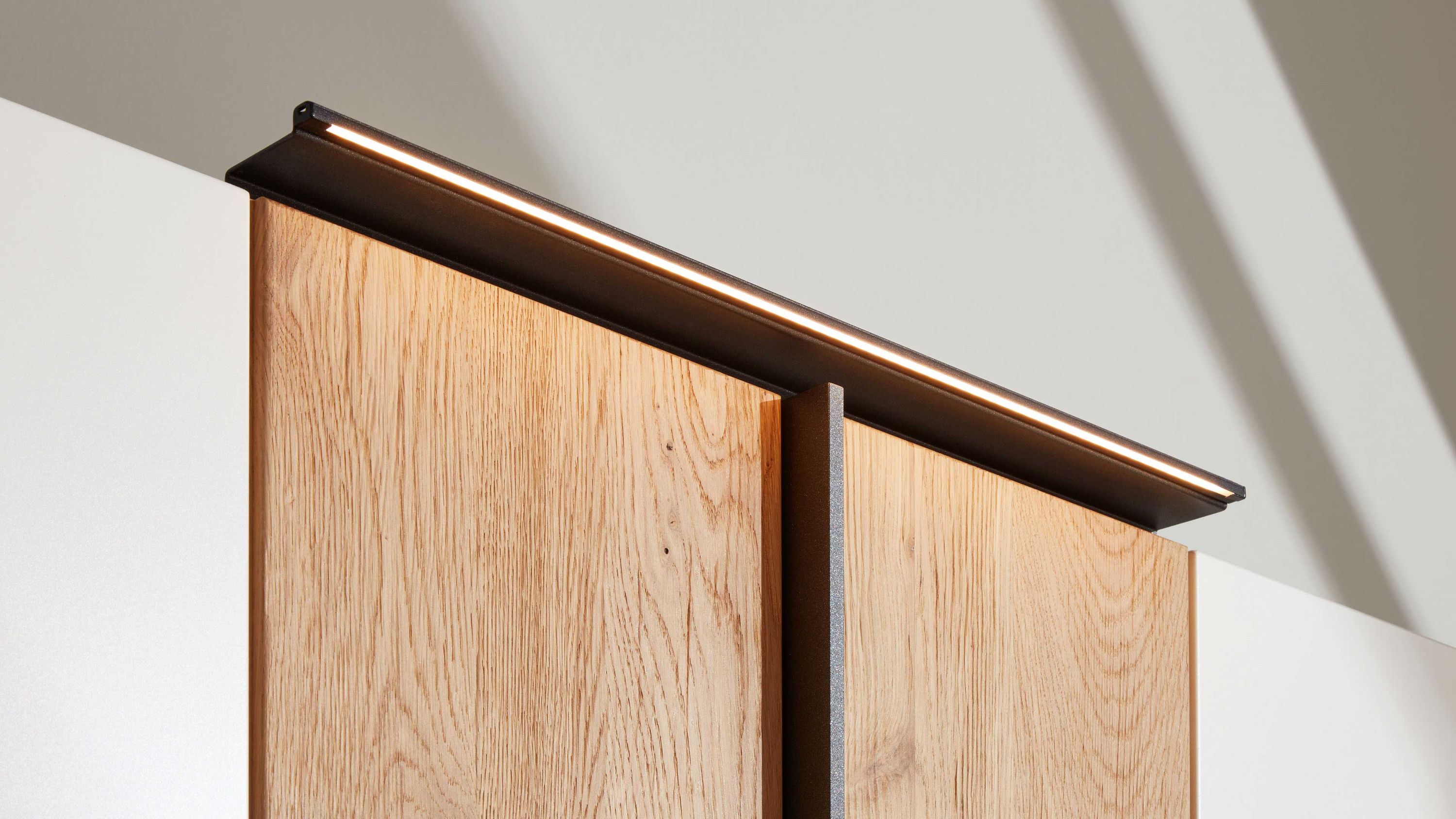 Schmale schwarze Aufbauleuchte mit warmweißem Licht auf einem Holzschrank