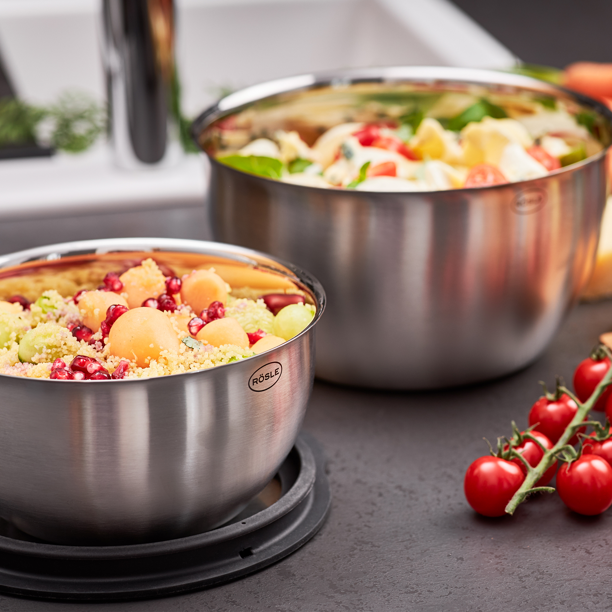 Zwei Edelstahlschüsseln mit Salat auf Küchenarbeitsplatte neben Spüle Cherrytomaten daneben leicht schräg von oben
